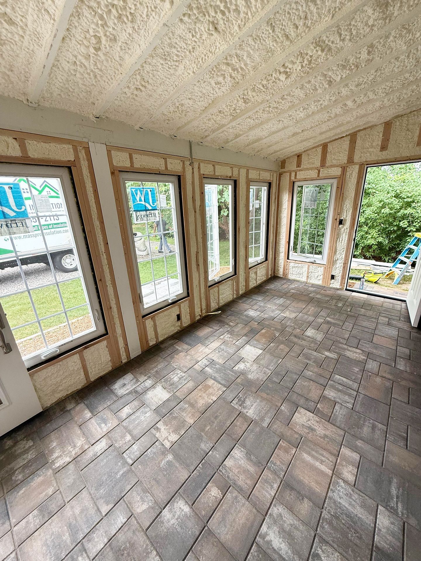 Interior sunroom with brick-style flooring, windows, and foam insulation on walls and ceiling.