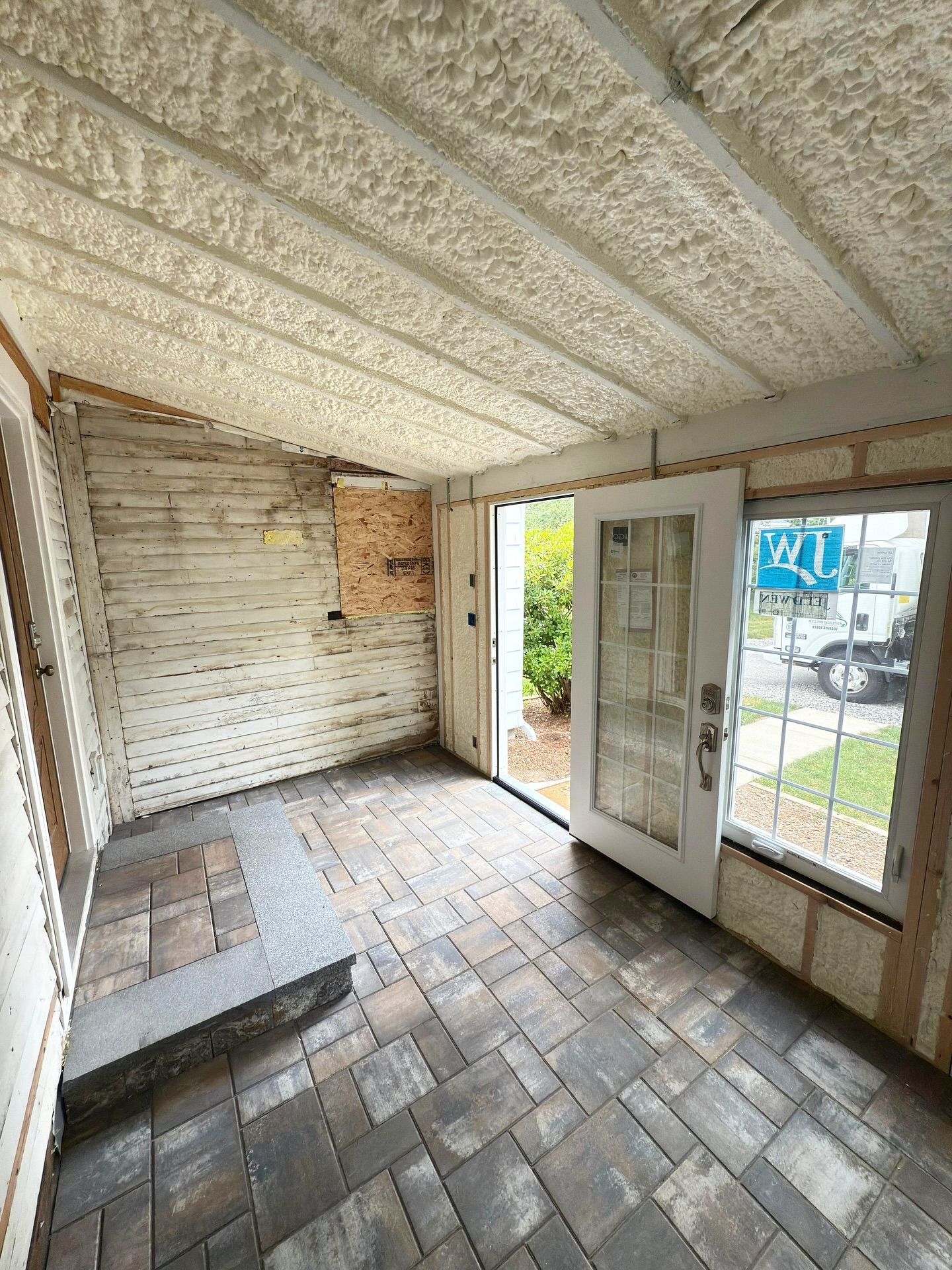 Sunroom under construction with brick floor, open doorway, white door, and insulated ceiling.