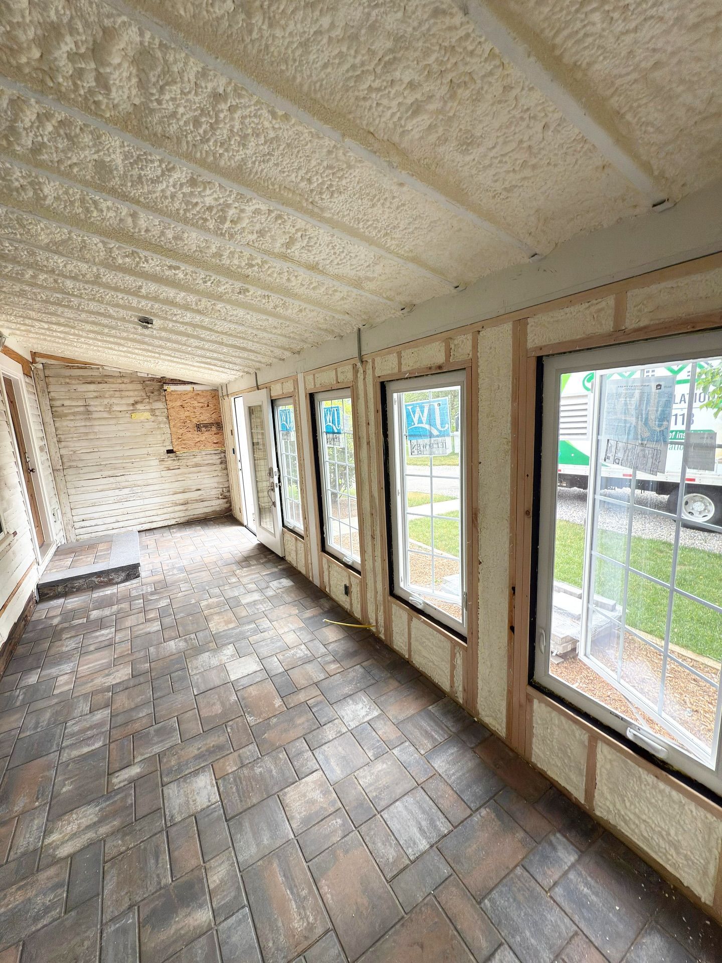Interior of a room with foam insulation on walls and ceiling, windows, and a brick-patterned floor.