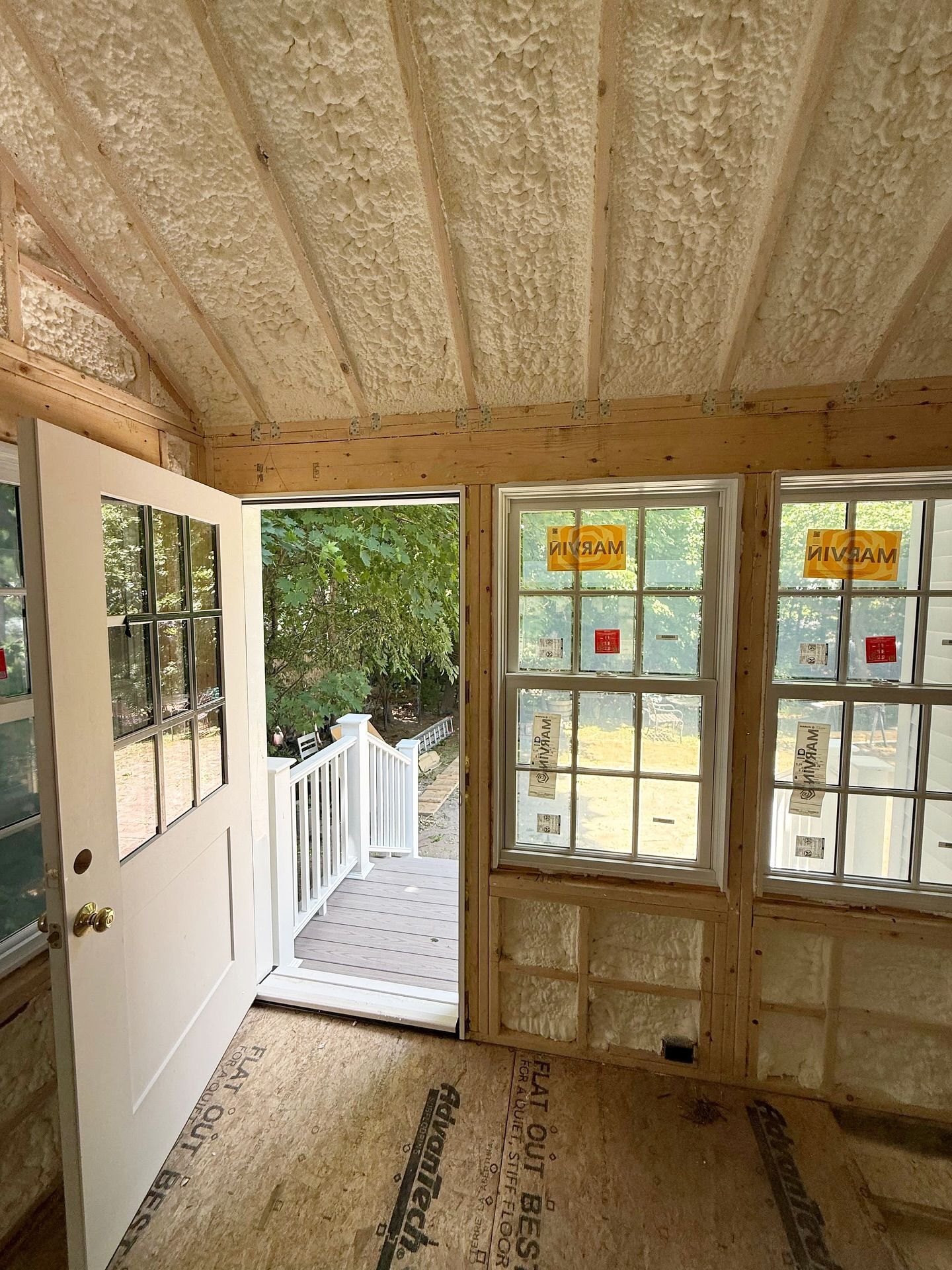 Interior of a sunroom under construction; white door open to a deck, windows on the right, exposed insulation.