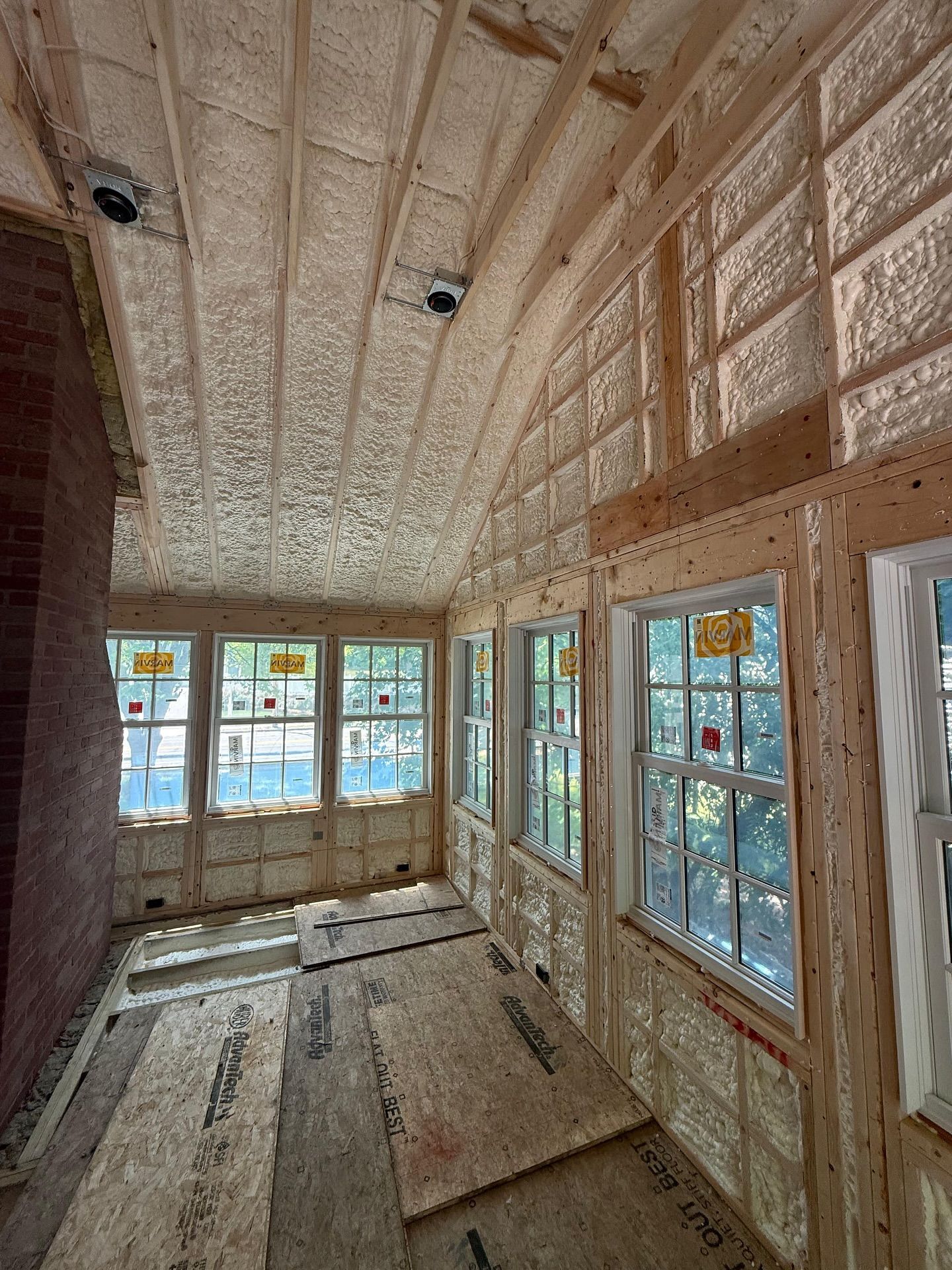 Interior of a room under construction: wood frame, windows, insulation, and a brick wall.
