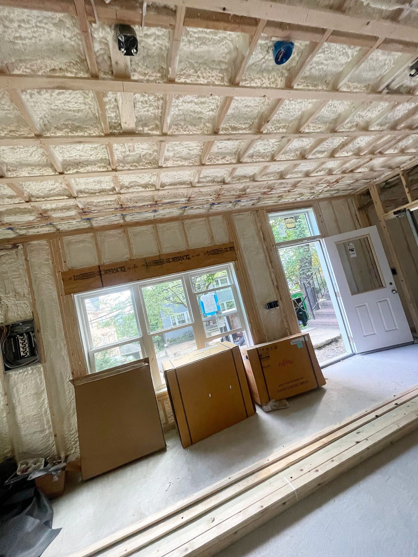 Interior construction with exposed beams, spray foam insulation, and boxes on the floor.