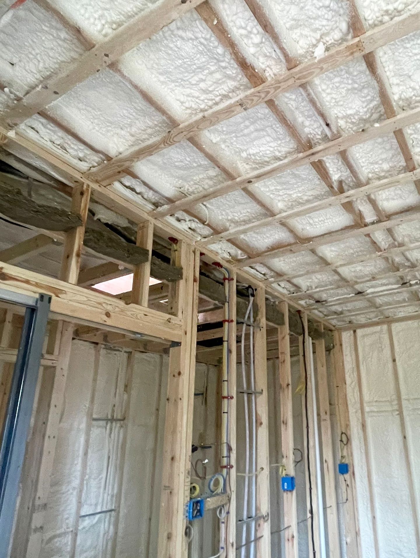 Interior of a building under construction with wooden framing and spray foam insulation visible on the ceiling and walls.