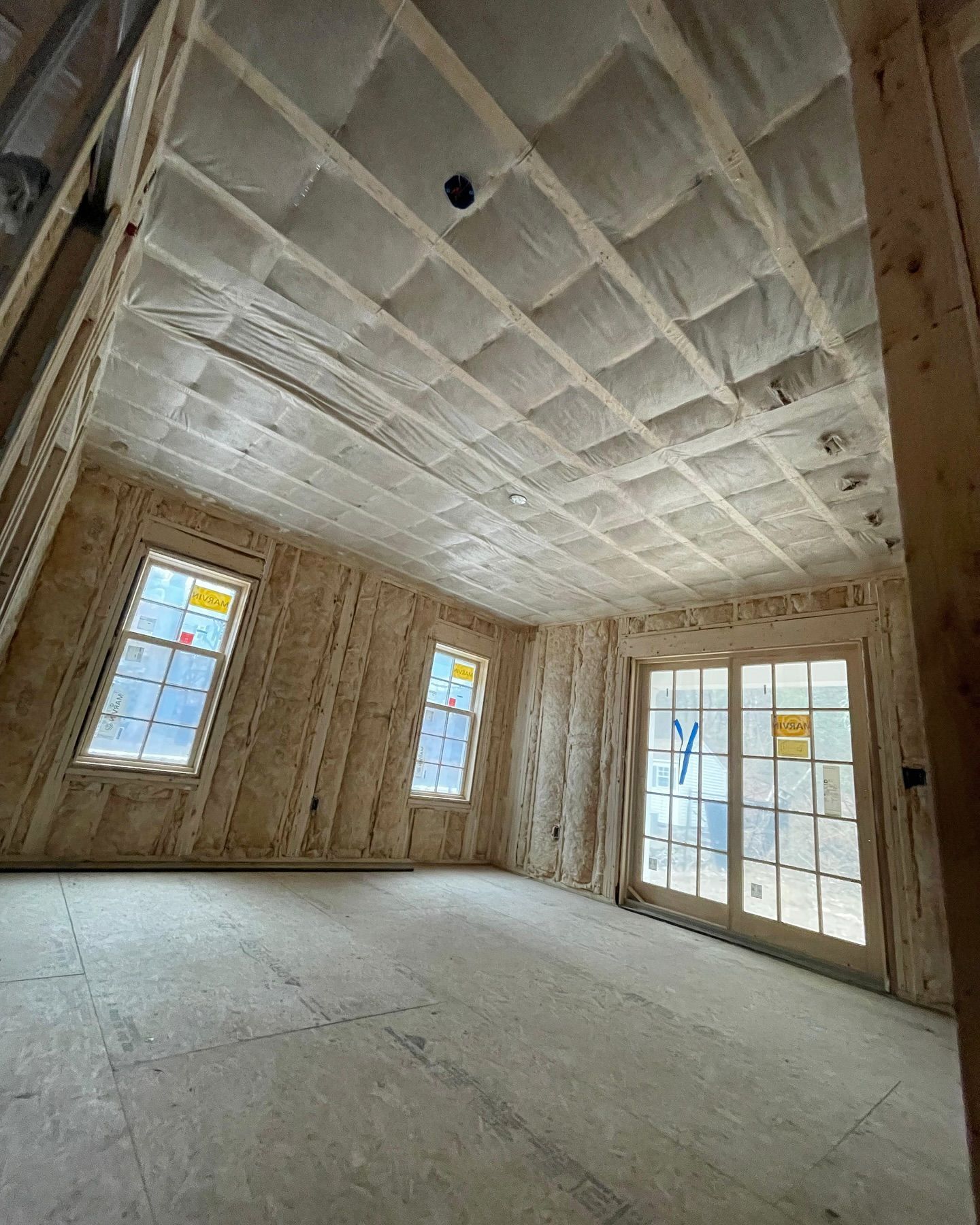 Unfinished room interior, wooden frame, windows, French doors, insulated ceiling.