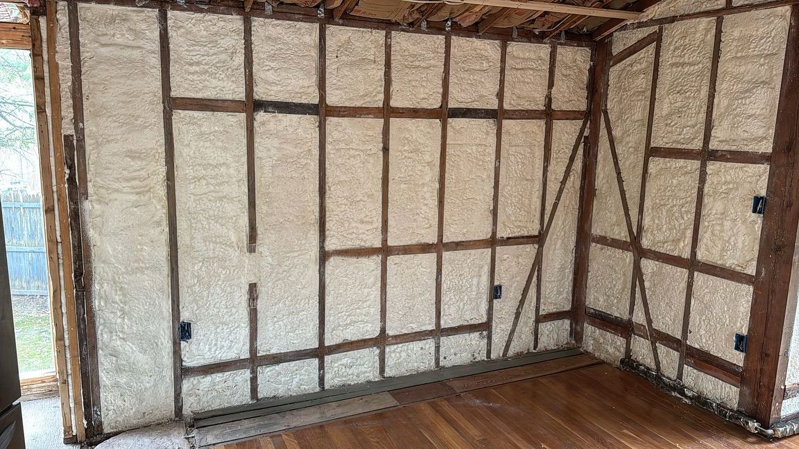 Interior of a room with wood frame walls filled with insulating material, wood floor, and outlets.