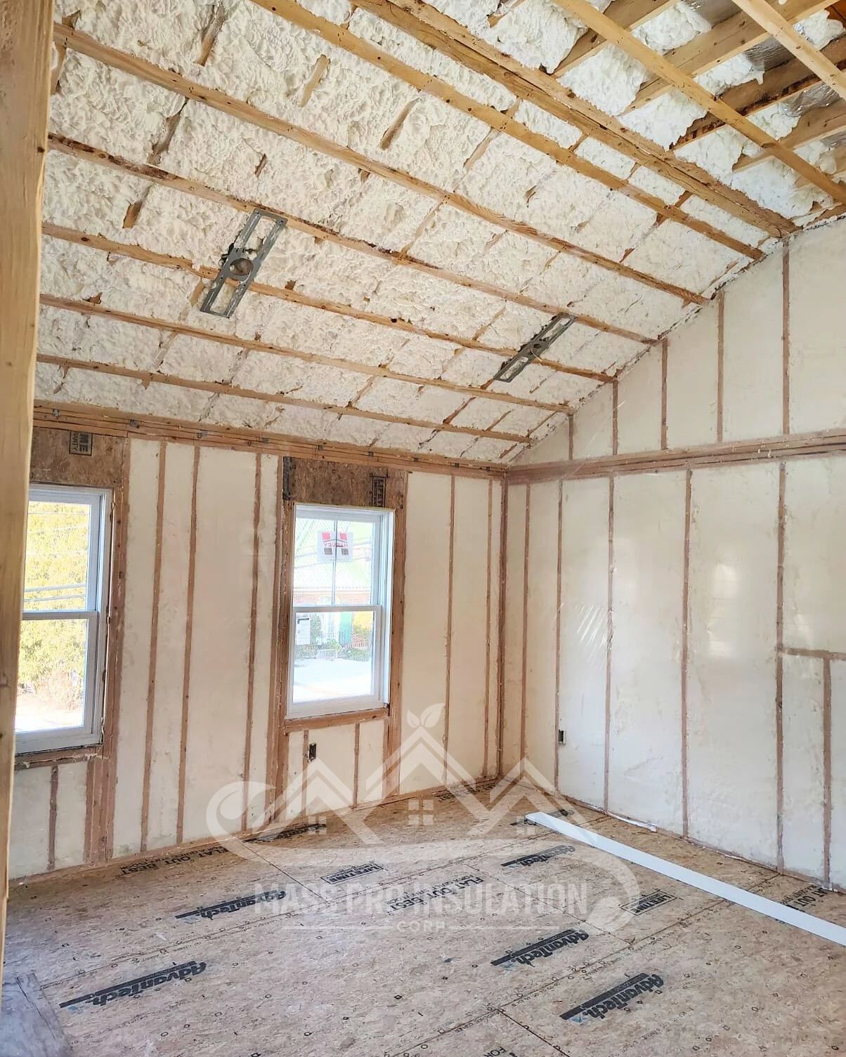Interior room with spray foam insulation on walls and ceiling, windows, and wooden framing.
