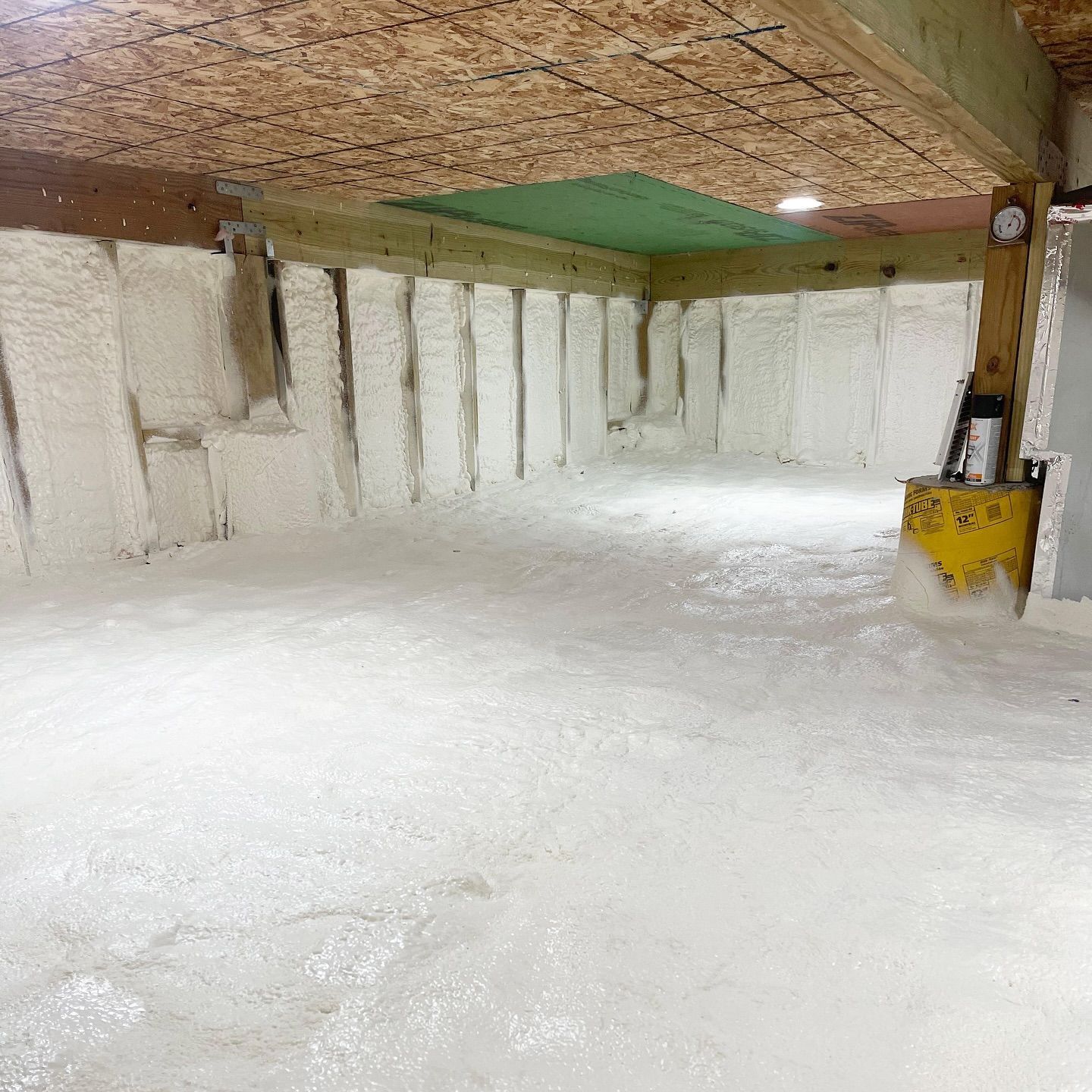 A basement being insulated with spray foam, covering the walls and floor. Beige-colored.