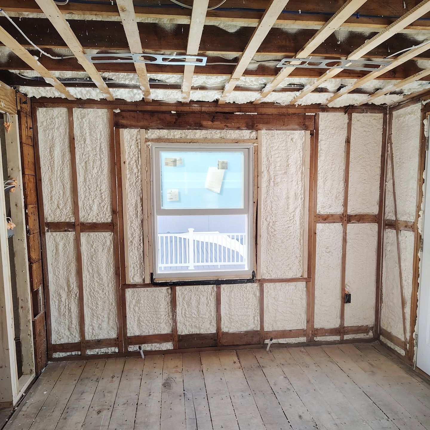 Interior room under construction, spray foam insulation between wooden studs, with a window.