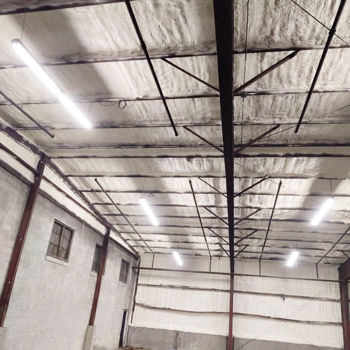 Warehouse interior with metal beams and panels, fluorescent lights, and insulated ceiling.