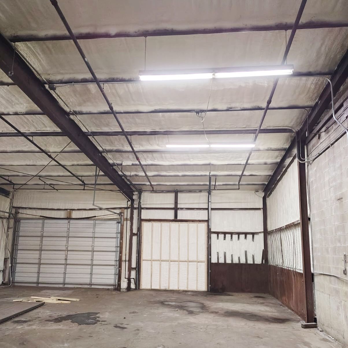 Empty warehouse interior with exposed metal beams, insulated ceiling, and a garage door.