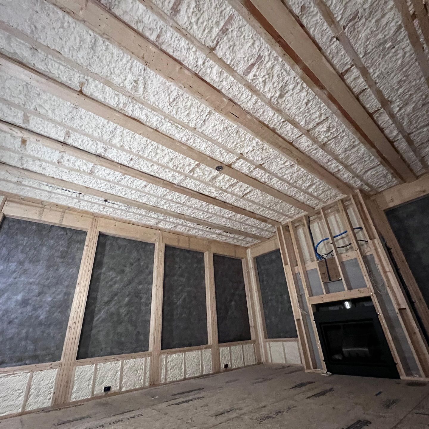 Interior view of a room under construction, with exposed wooden beams and spray foam insulation.