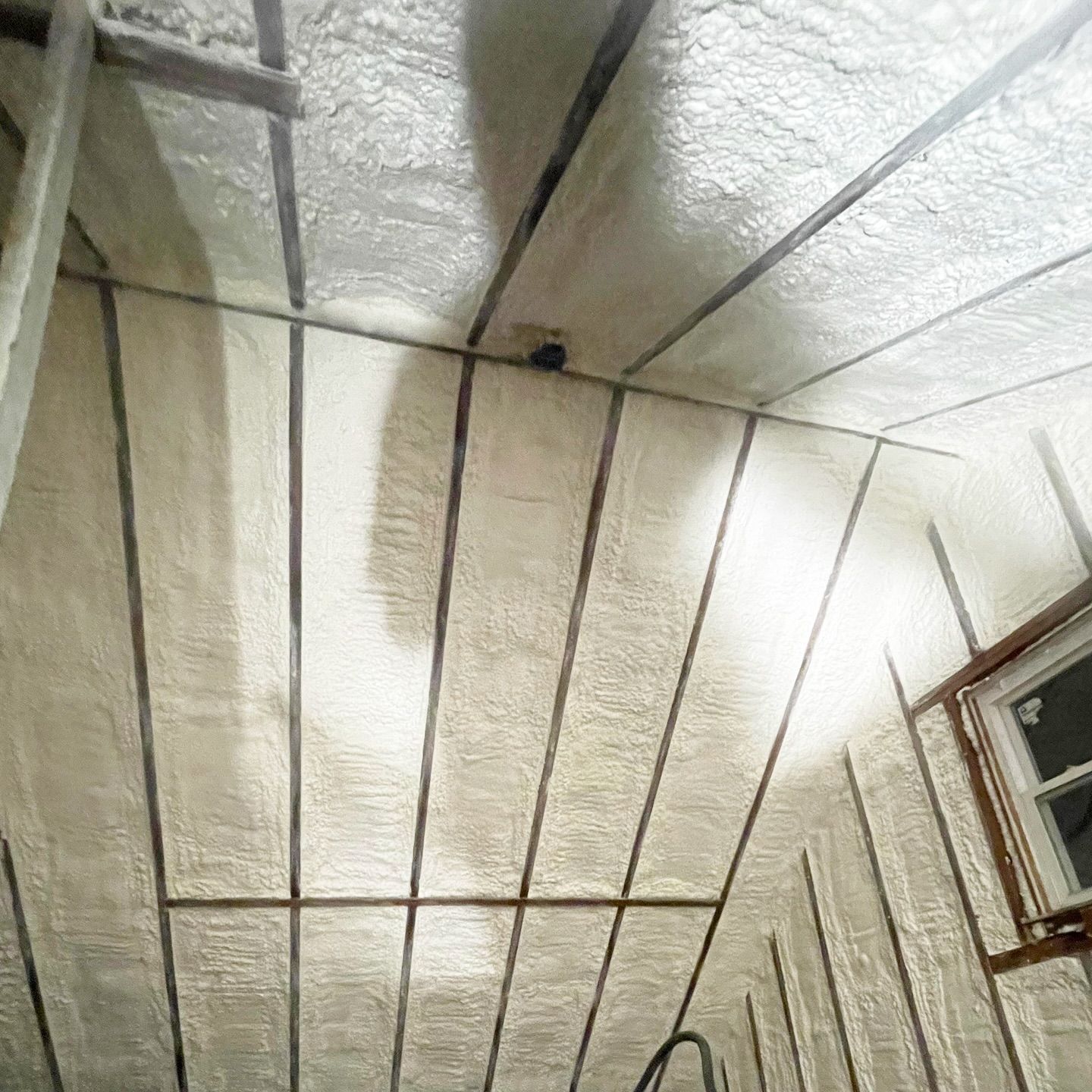 Attic interior with spray foam insulation between rafters; white and light brown colors.