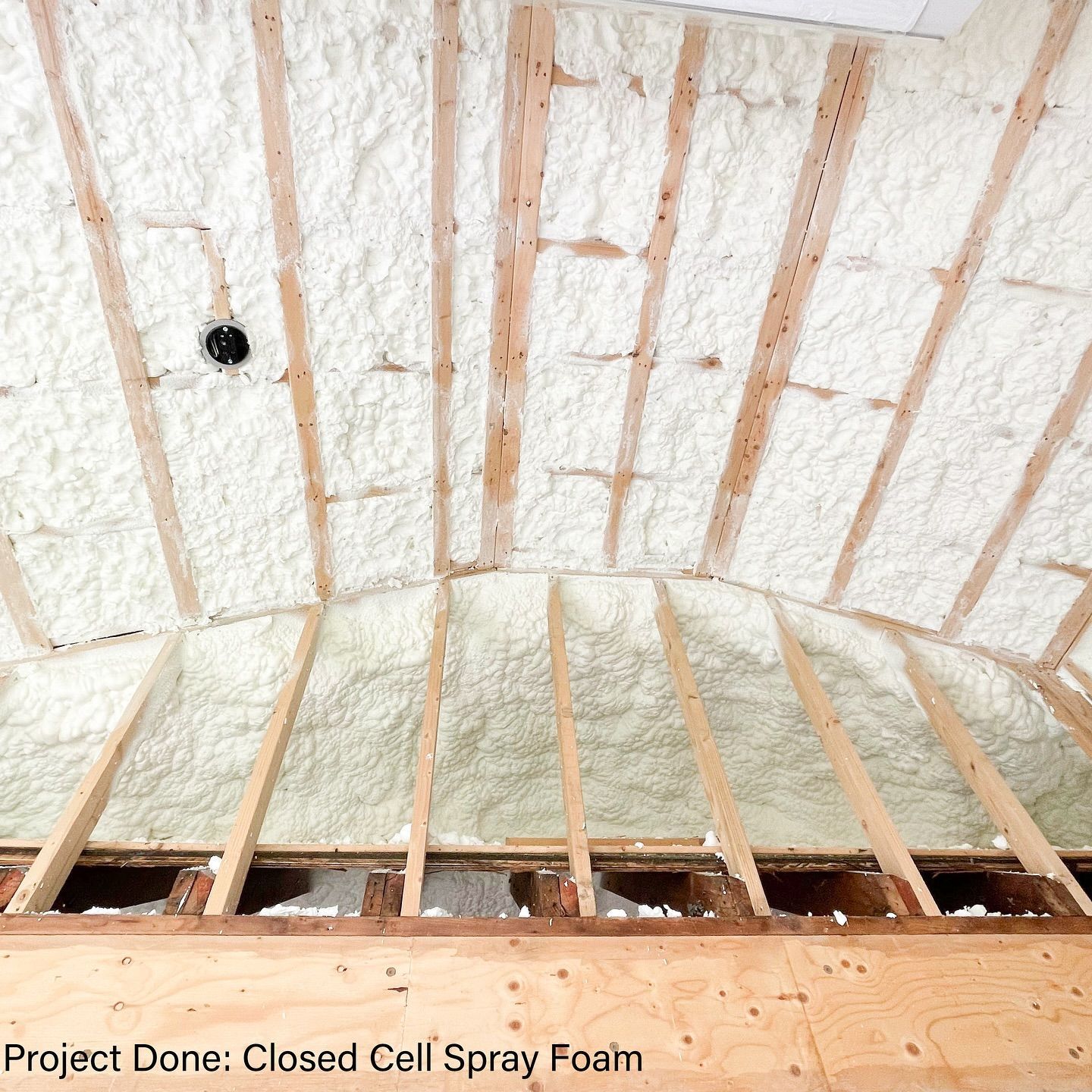 Spray foam insulation applied to an arched ceiling, with wooden beams visible.