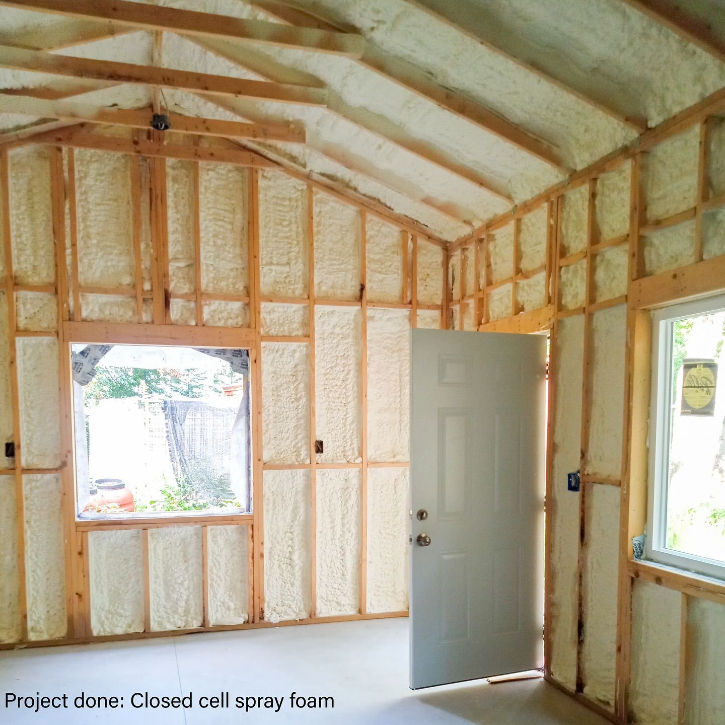 Interior of a building being insulated with closed-cell spray foam on walls, ceiling, door, and window frames.