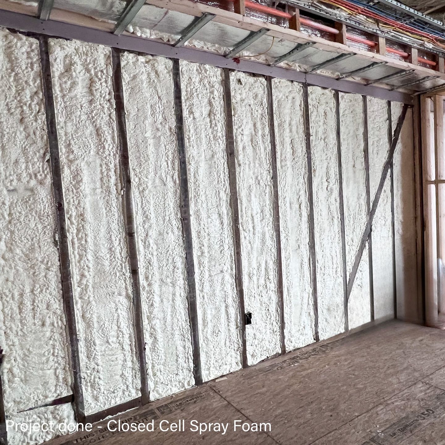 Wall with closed-cell spray foam insulation between vertical beams in a building under construction.