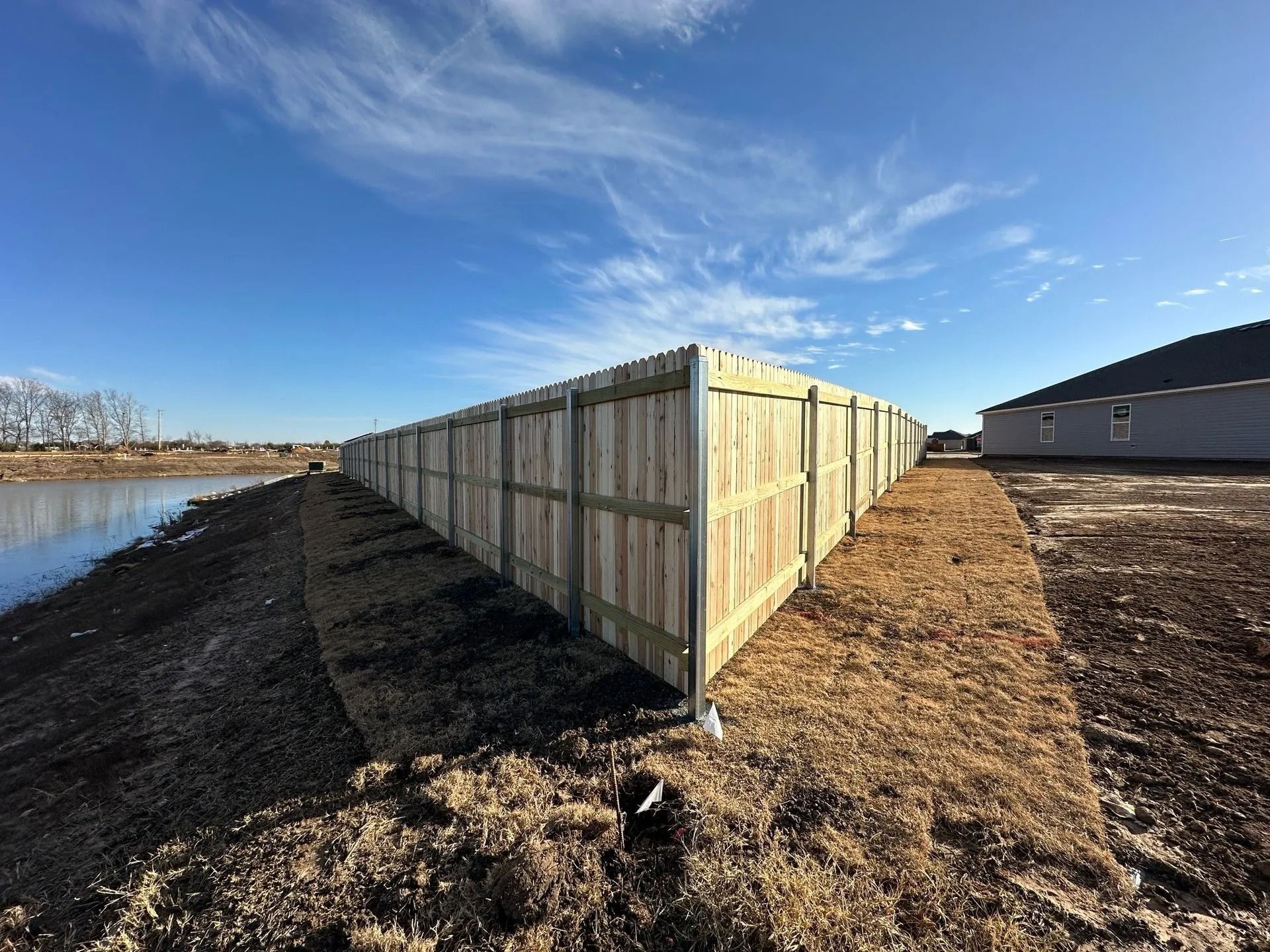 Wooden fence bordering a body of water and a grassy area under a blue sky.