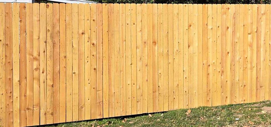 Black metal sliding gate in front of a white wall, set between two black pillars on a gravel surface.