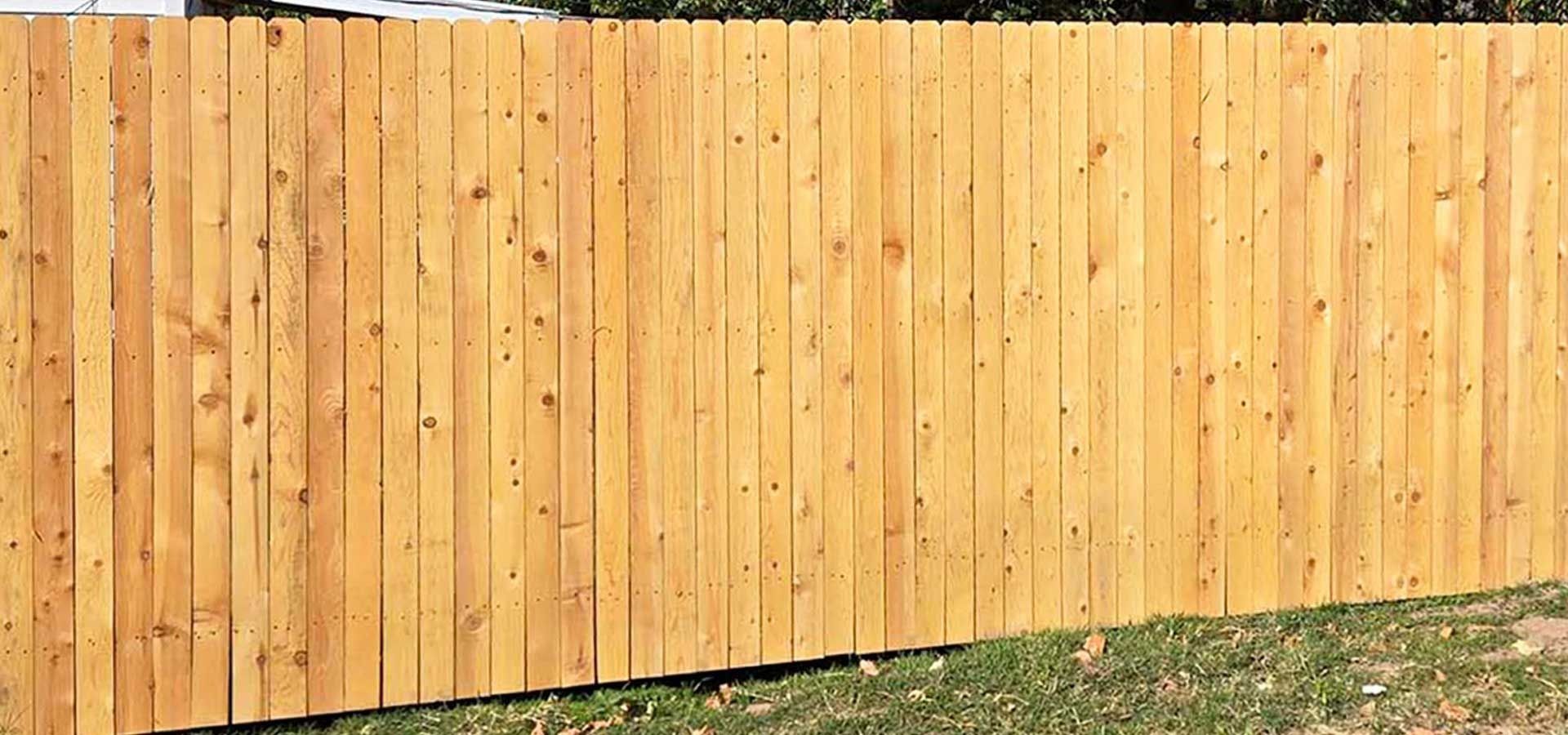 Black metal sliding gate in front of a white wall, set between two black pillars on a gravel surface.