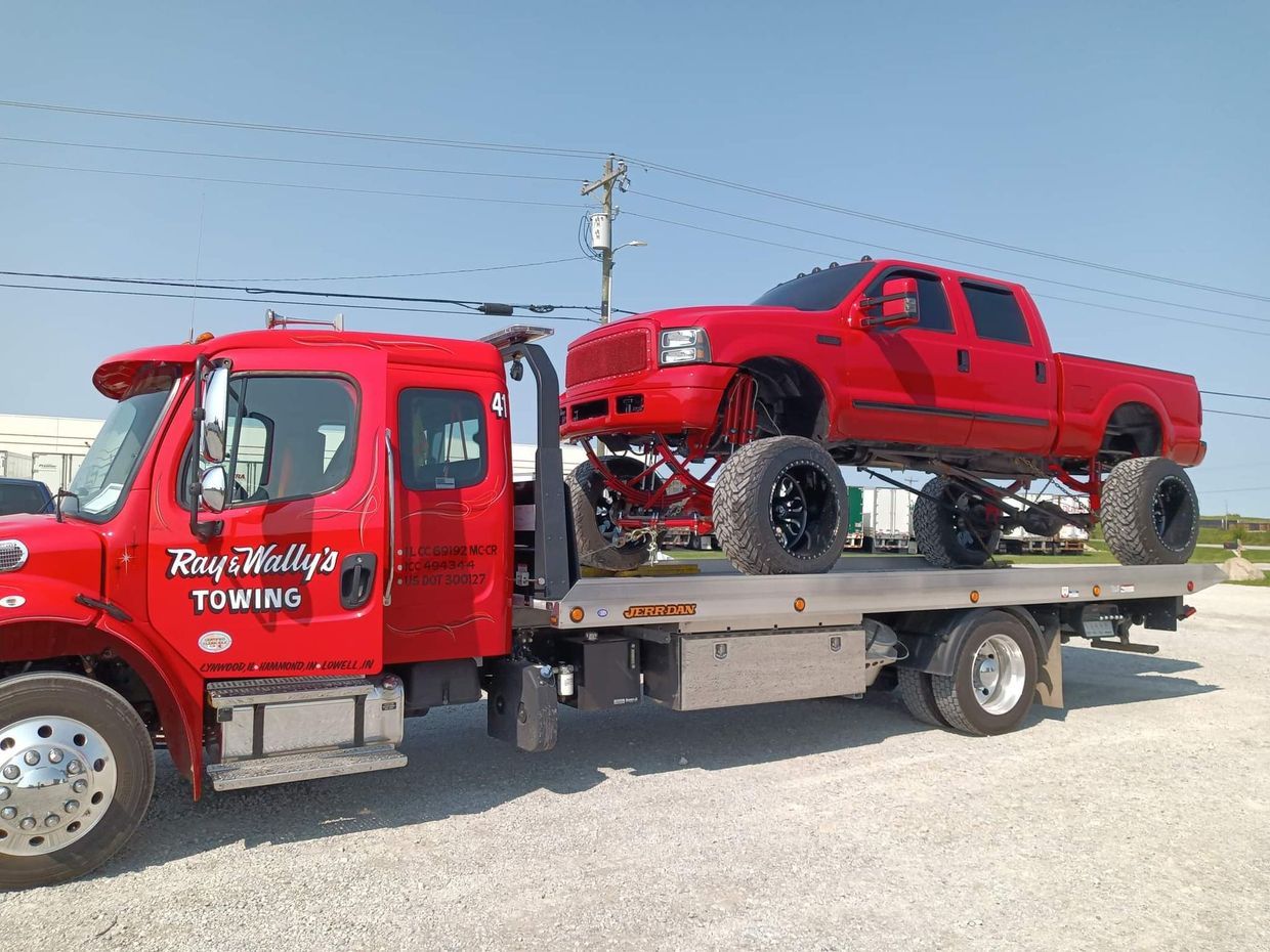 Red tow truck carrying a red lifted pickup truck on a sunny day.