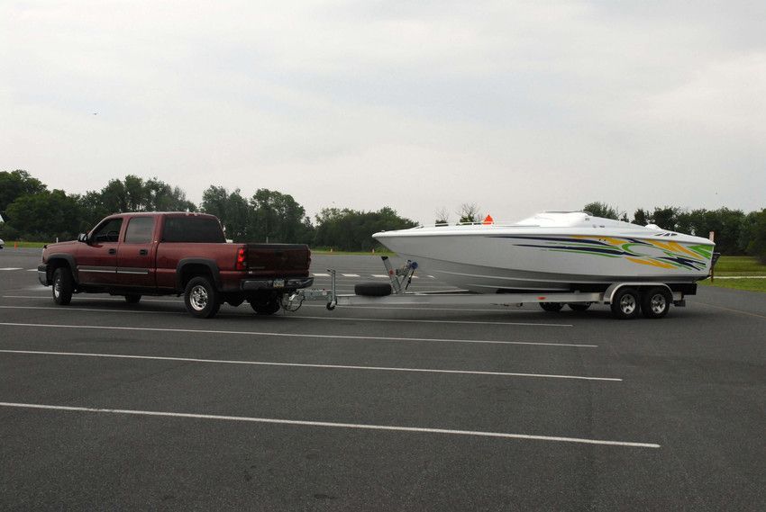 Red pickup truck towing a white speedboat on a trailer in a parking lot