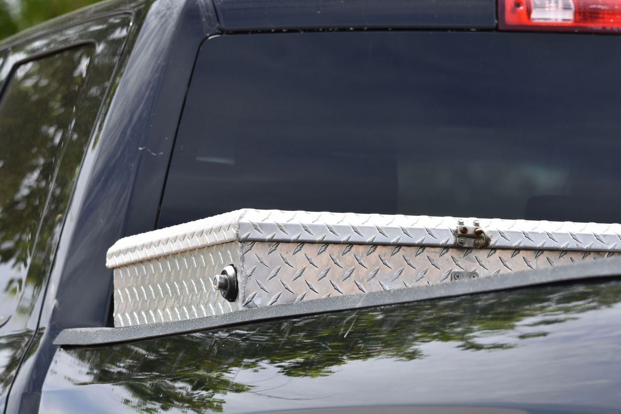 Silver diamond-plate toolbox mounted on the front of a black pickup truck.