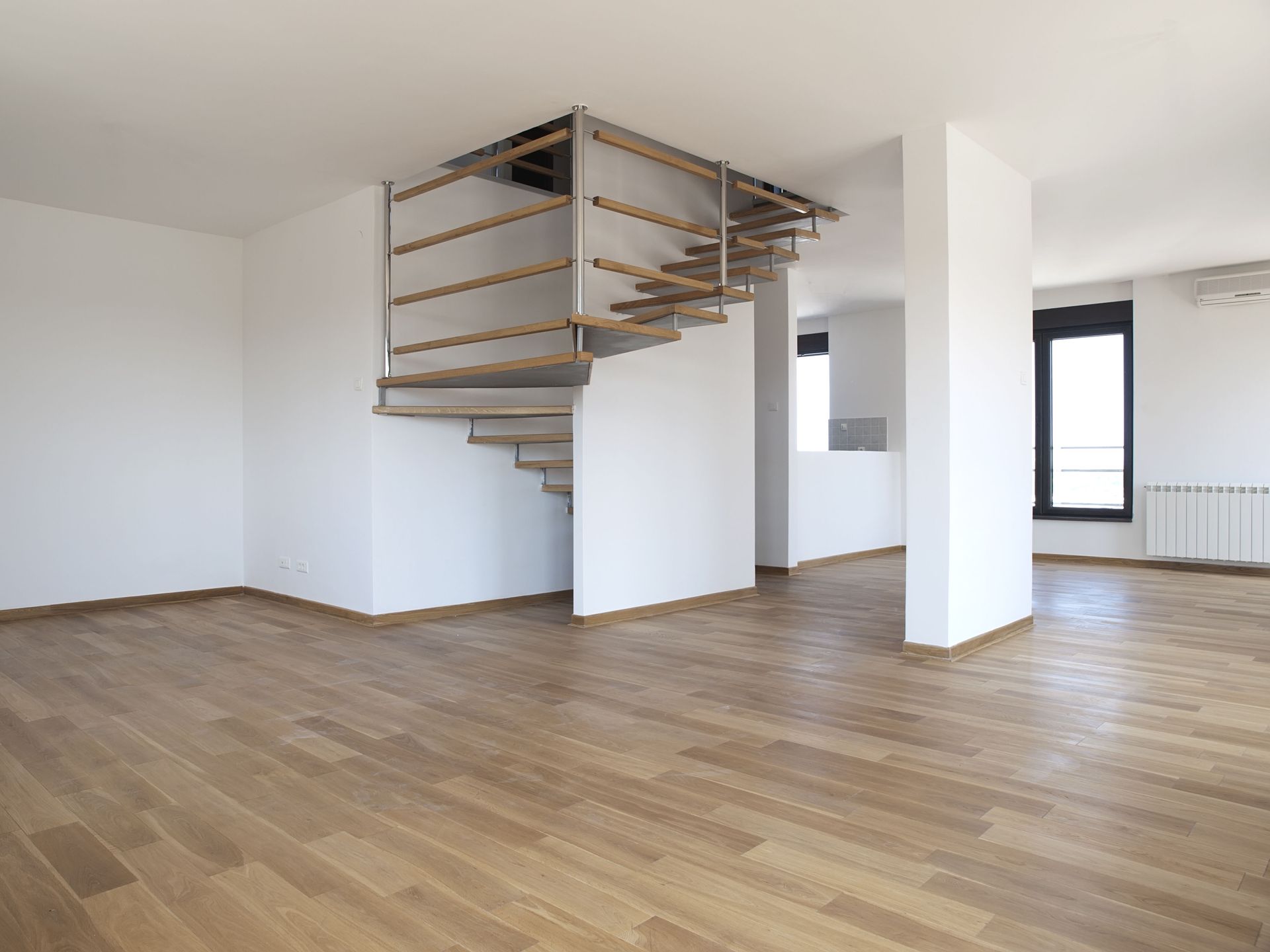 Empty modern apartment with wood floors, white walls, and a floating staircase divider