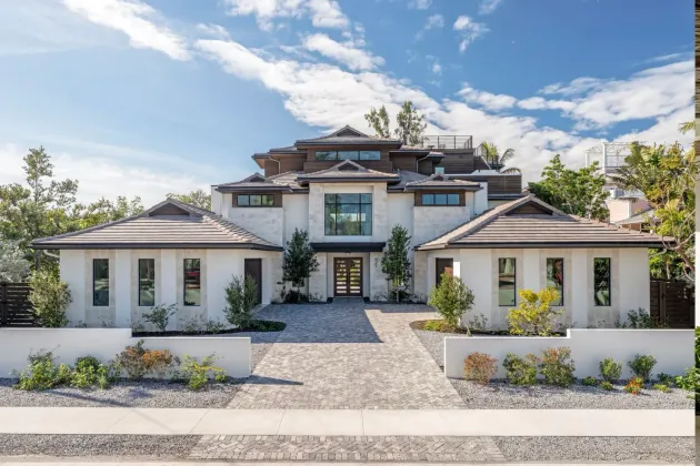 Modern white luxury house with a gravel driveway, flat roofs, and a bright blue sky
