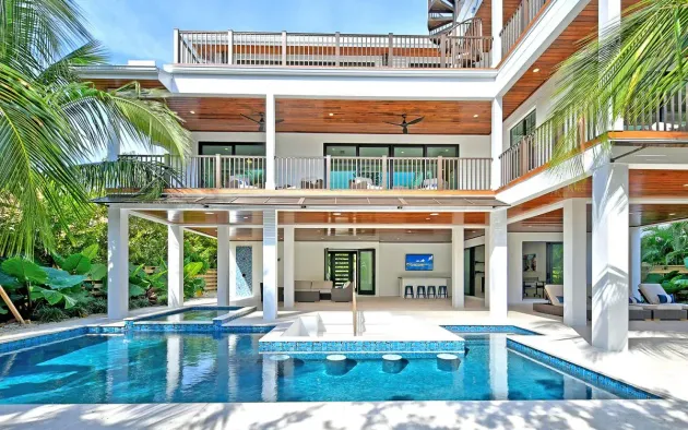 Modern tropical villa with a blue pool, white balconies, and palm trees