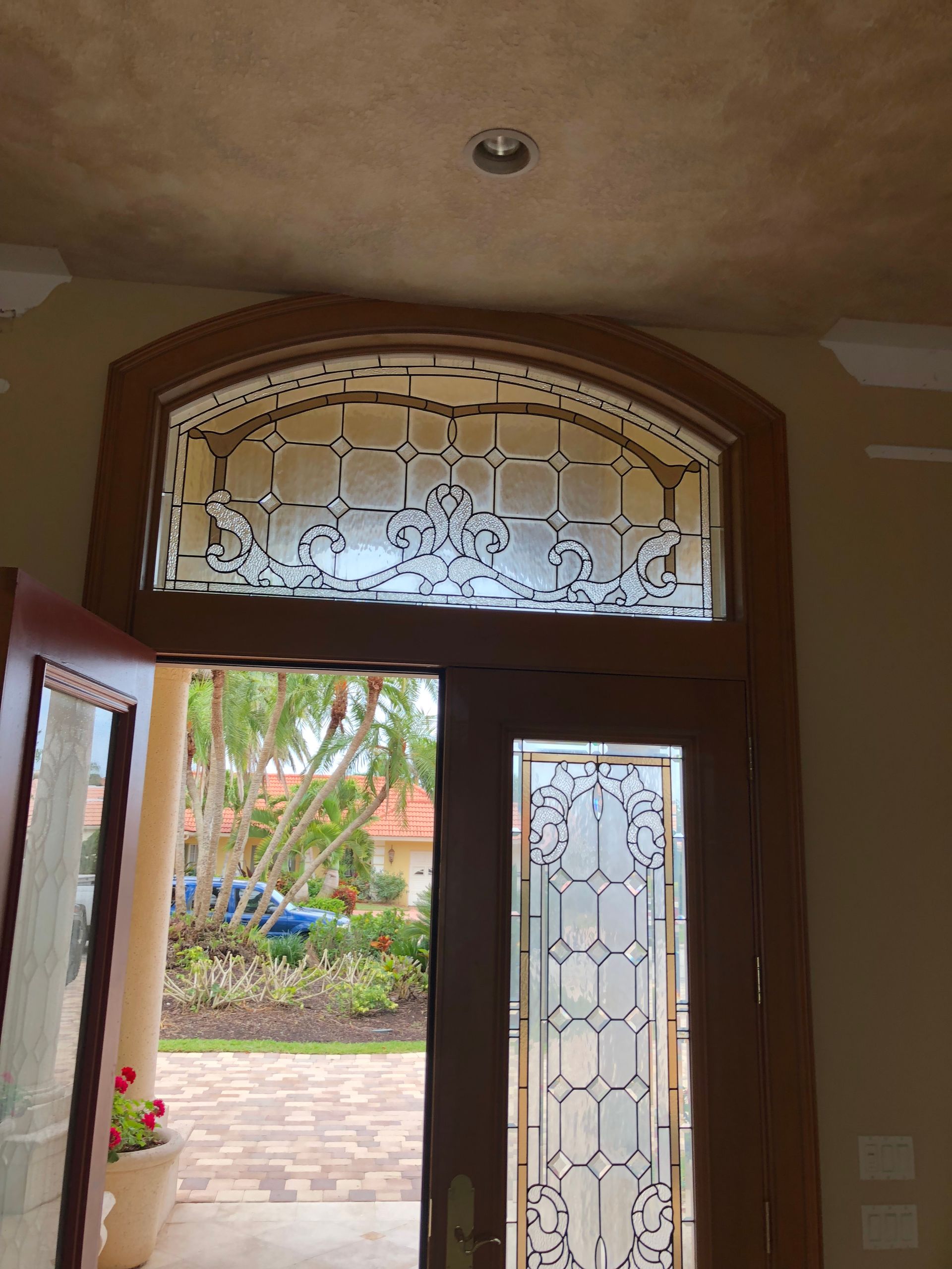Open front door with frosted glass panels, showing a bright courtyard outside.