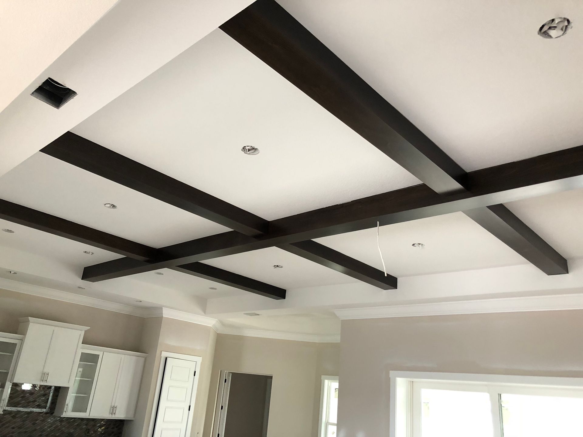 Interior ceiling with dark exposed beams and recessed lights above a bright room.
