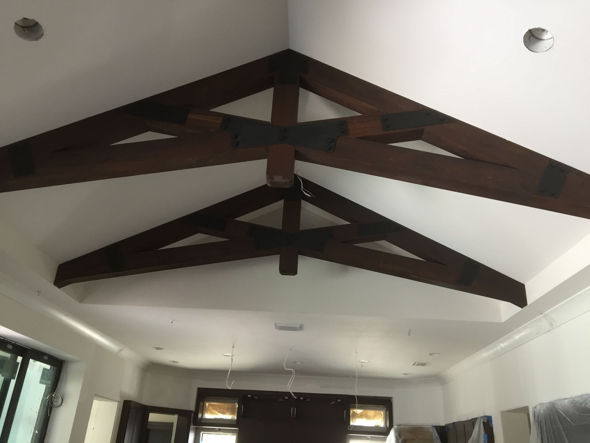 Ceiling with dark wooden exposed beams and recessed lights in a white room