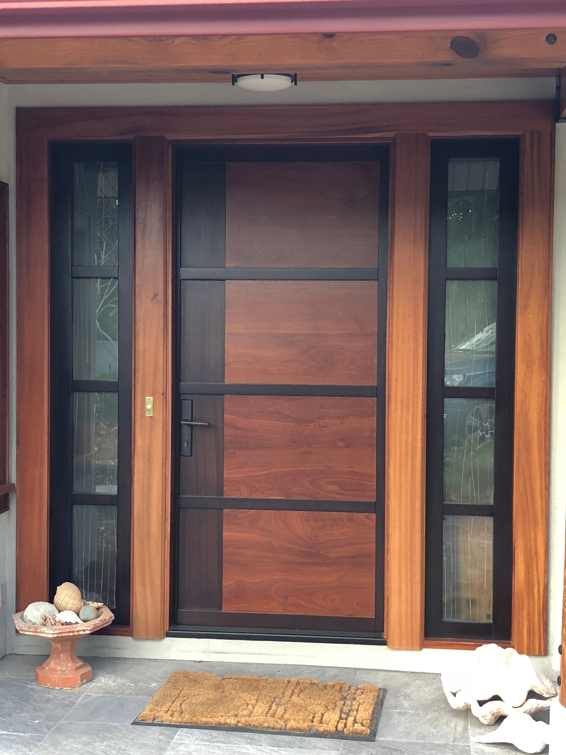 Front entrance with a wooden door, sidelights, welcome mat, and decorative bowls on a stone porch.