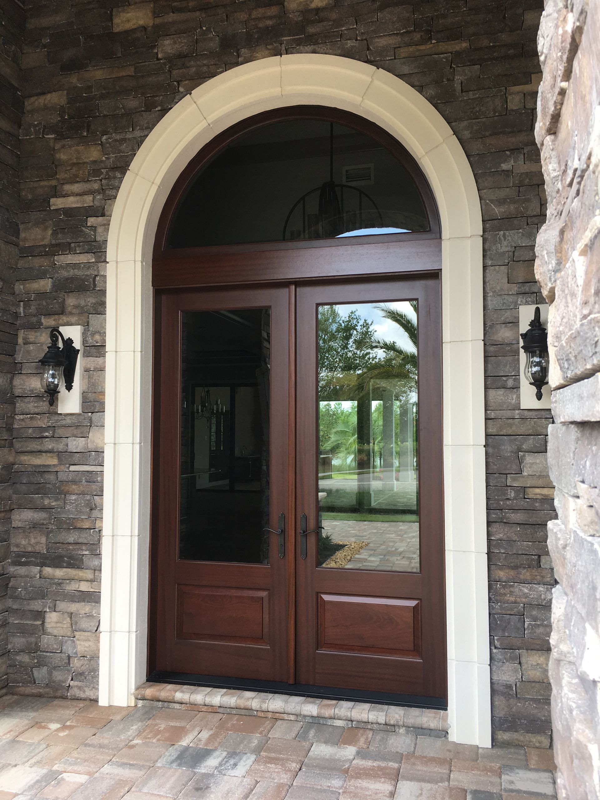 Stone entryway with arched brown double doors and glass panels under a brick archway