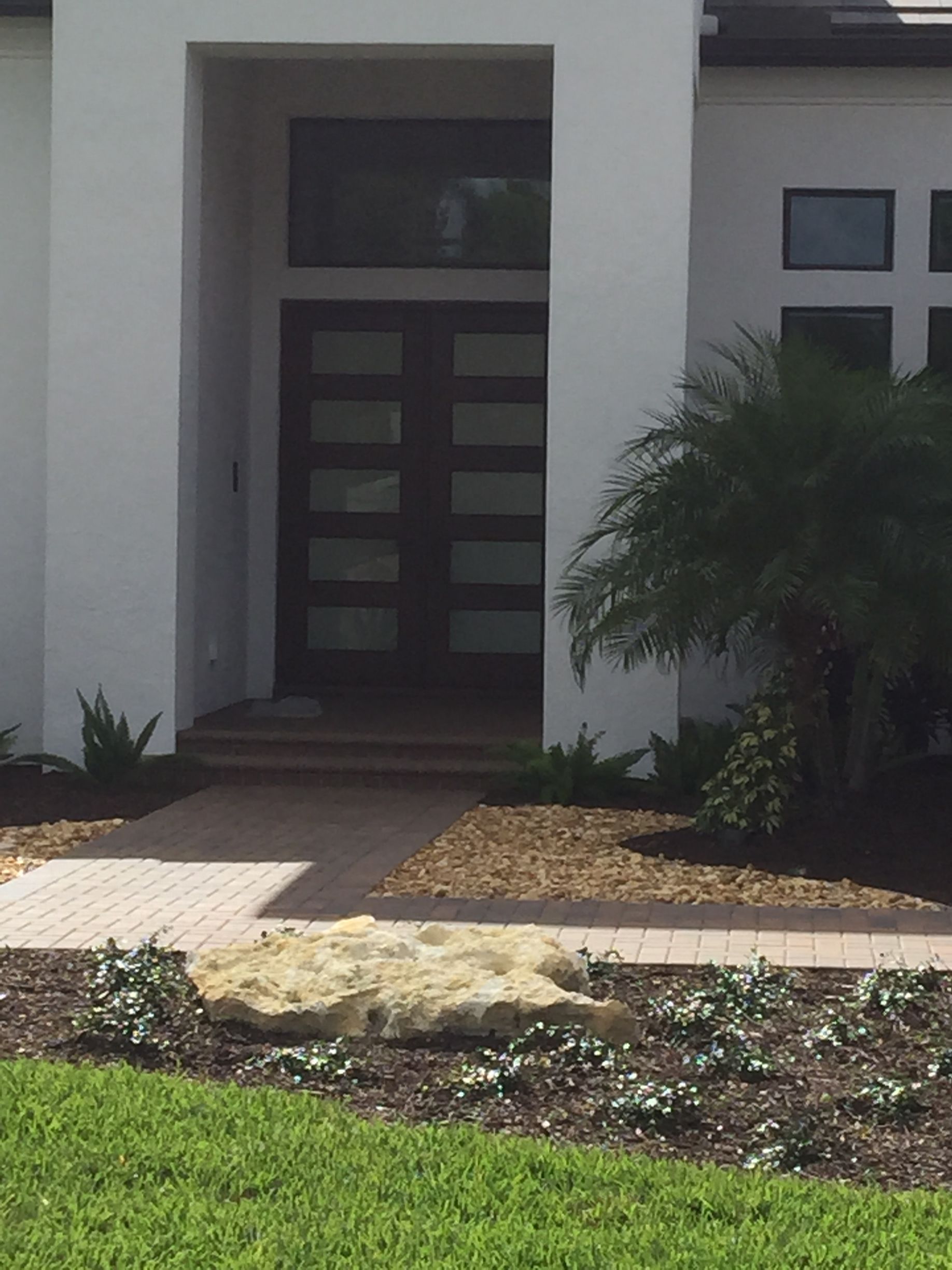 Front entrance of a modern house with a dark wooden door, white columns, and a small garden path.