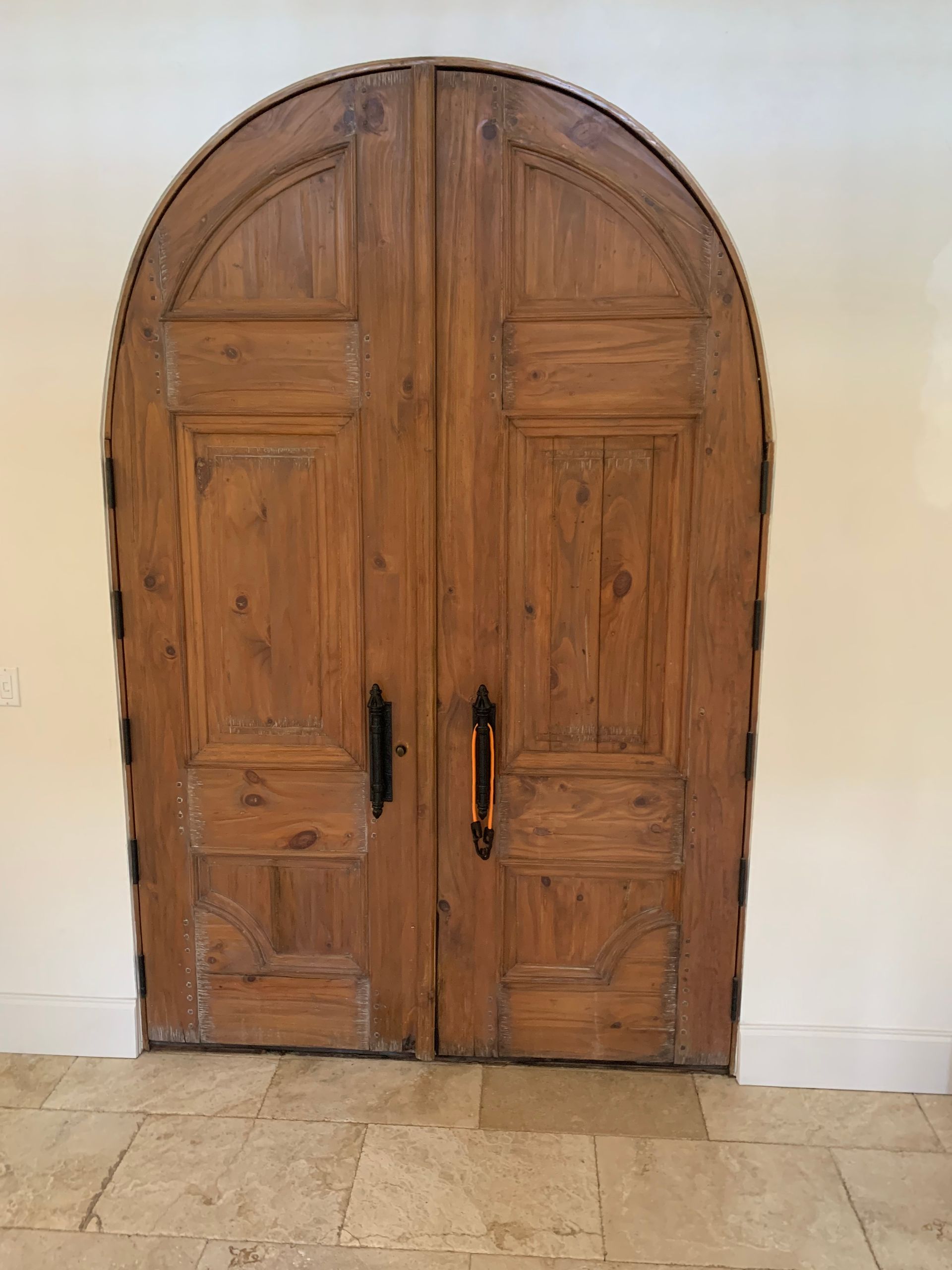 A pair of arched wooden double doors with black handles in a beige wall