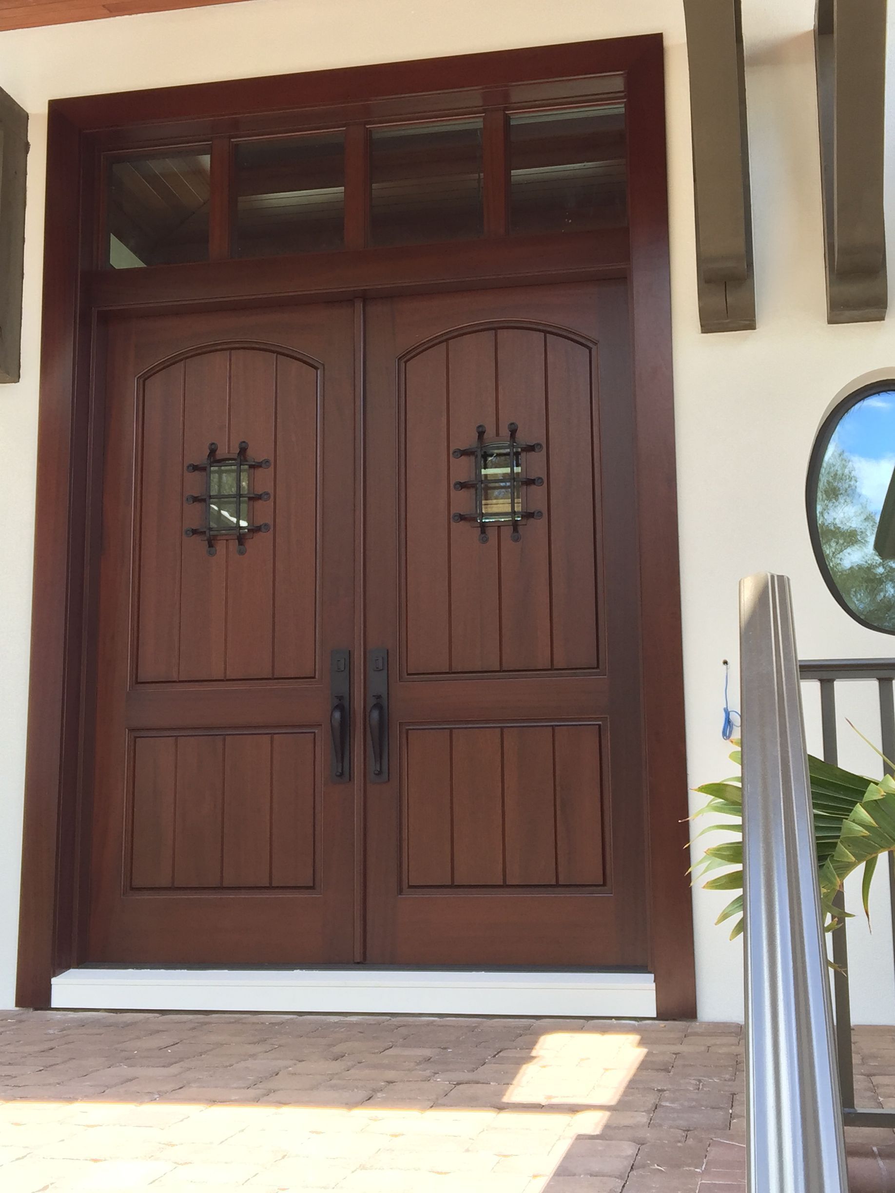 Wooden double front doors with decorative glass panels and black handles at an entrance.