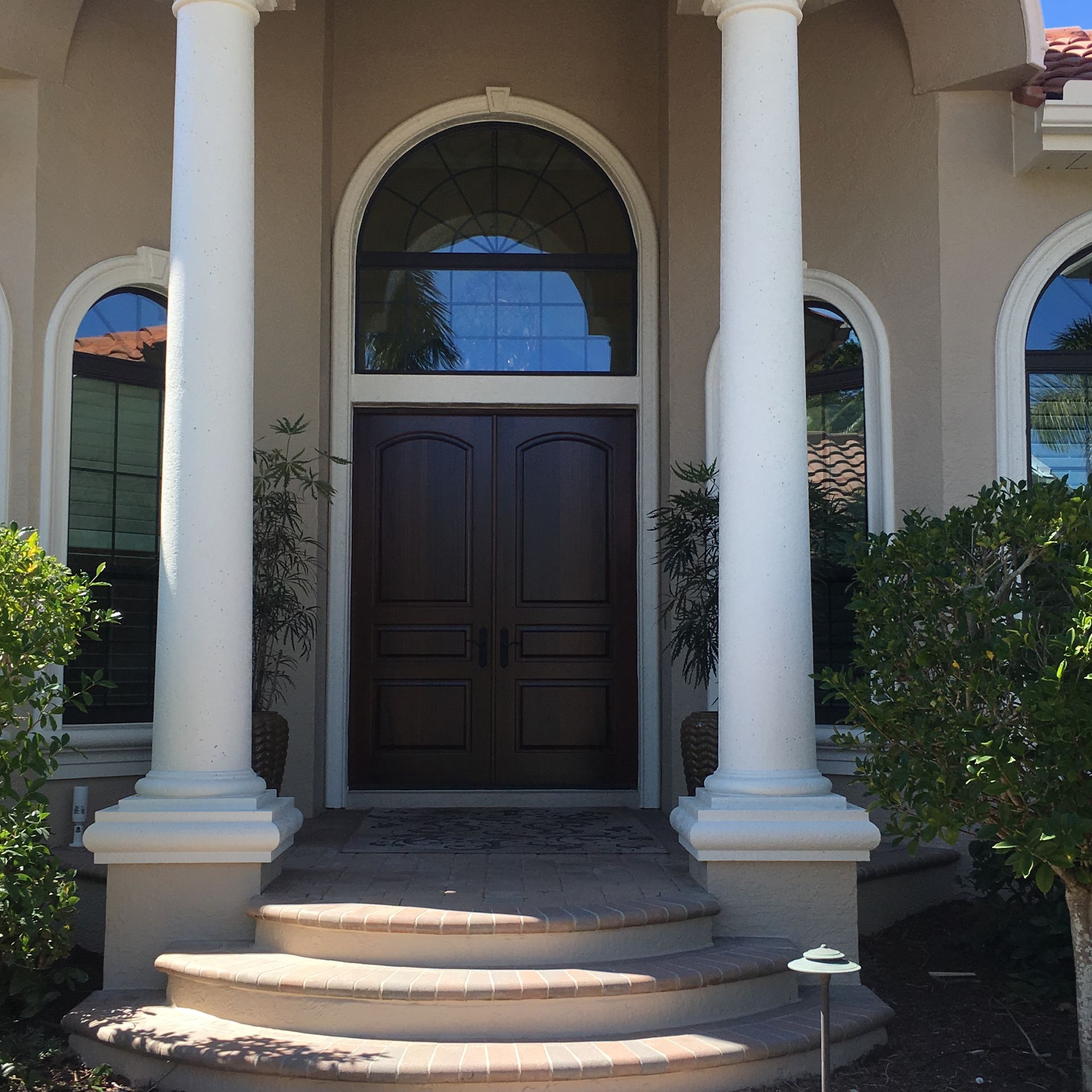 Front entrance with dark double doors, white columns, arched window, and curved steps