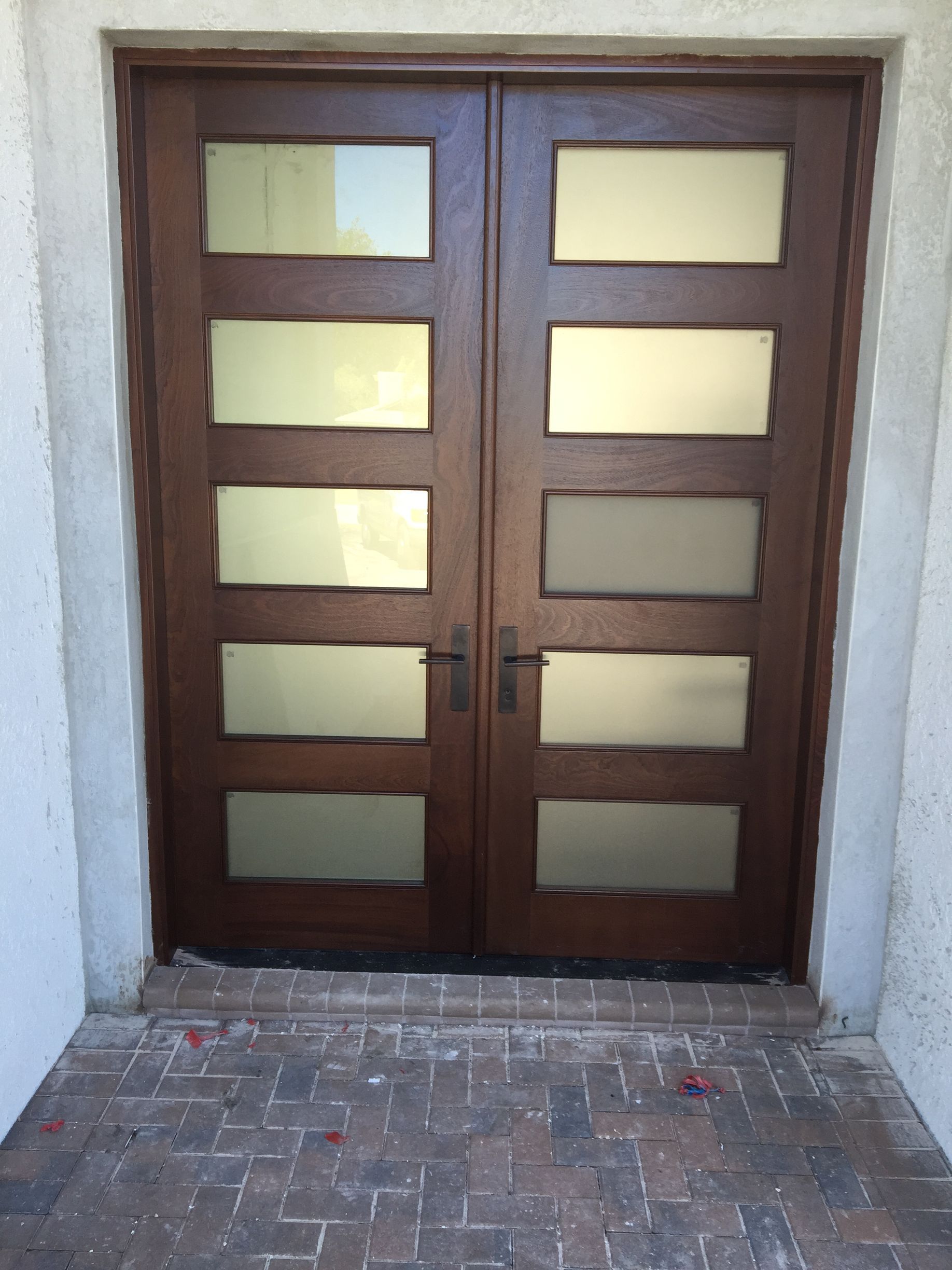 Wooden double front door with frosted glass panels and a brick-paved entryway