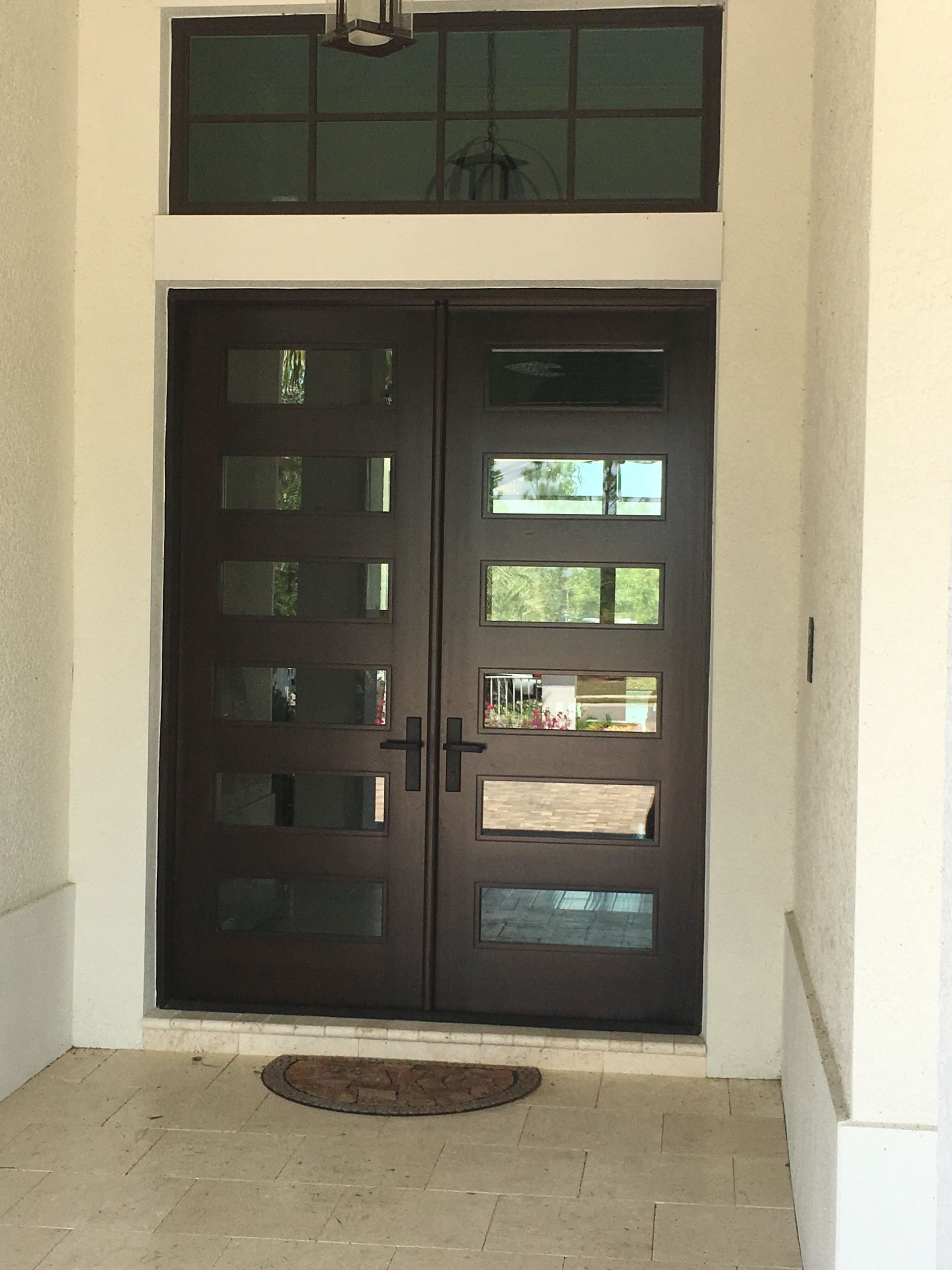 Front entrance with dark double doors, narrow window panes, and a doormat in a cream-colored entryway
