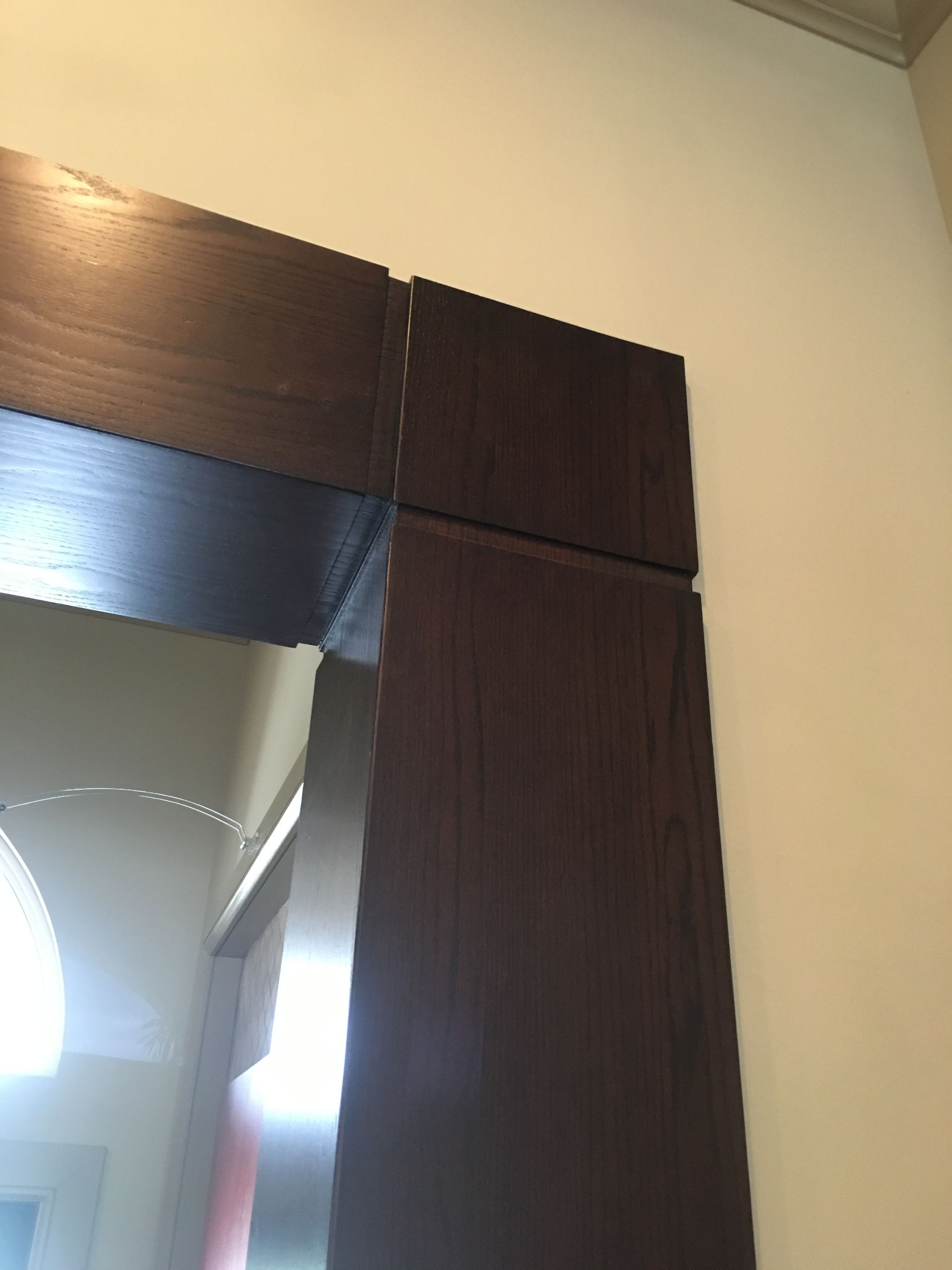 Dark wood trim framing a doorway against a cream wall, with bright light beyond the opening