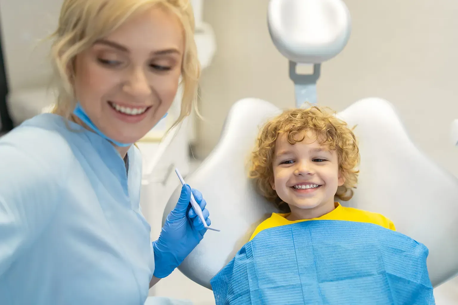 Dentist smiling at a child patient in a dental chair; dental examination in progress.