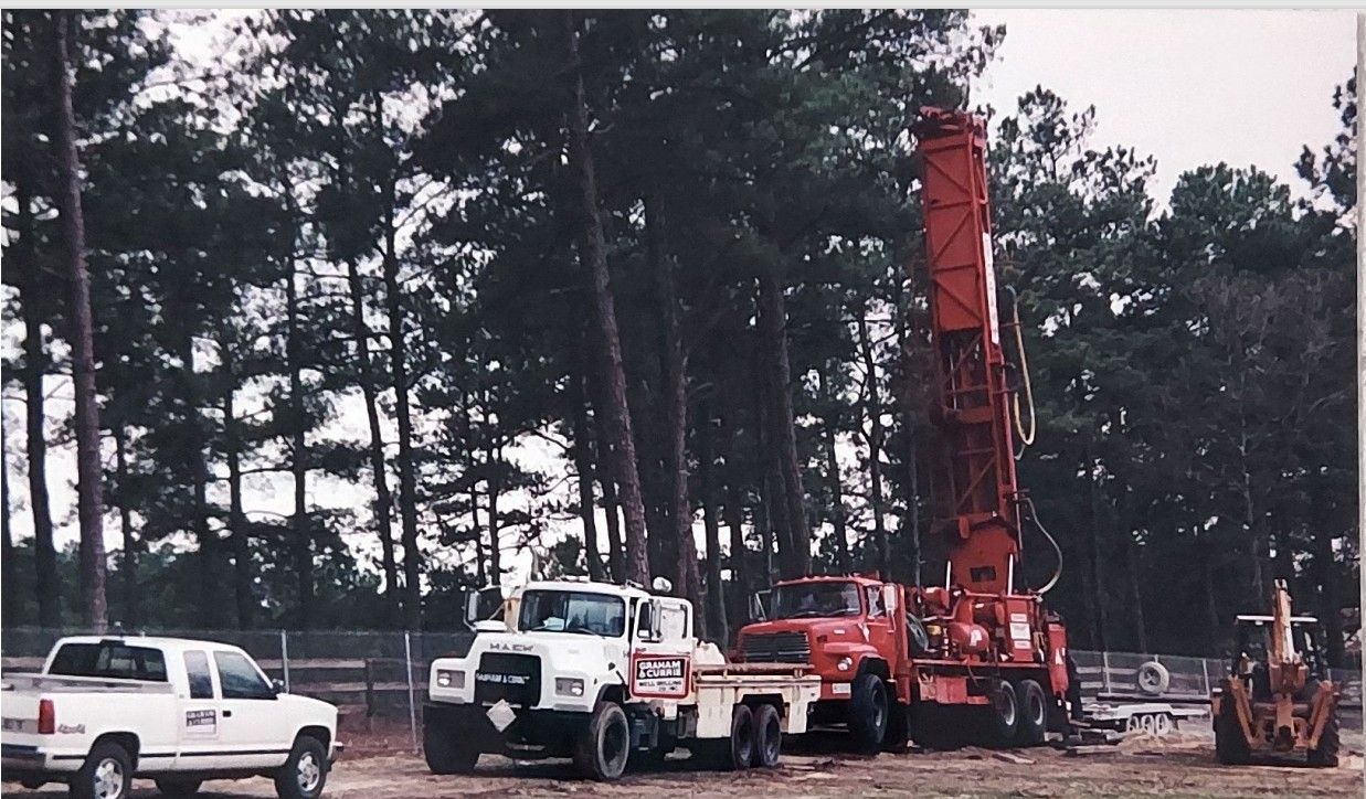Several trucks are parked in a field with trees in the background.