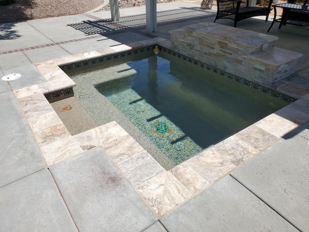 A small swimming pool is surrounded by tiles on a patio.