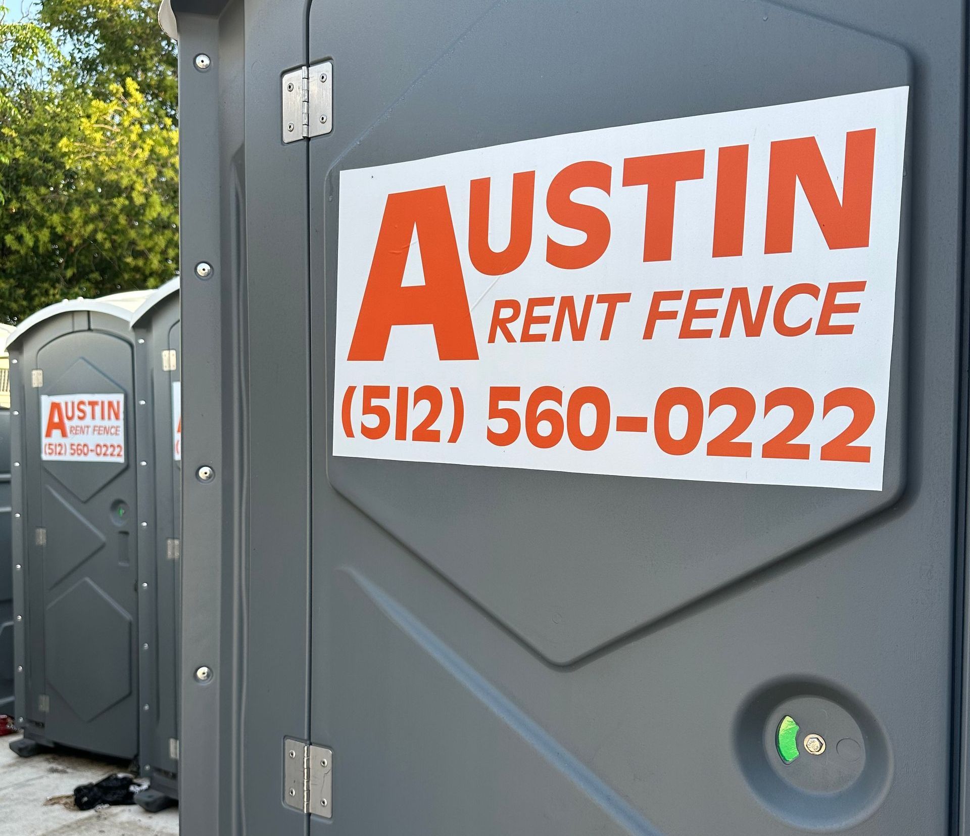 A sign for austin rent fence is on a portable toilet