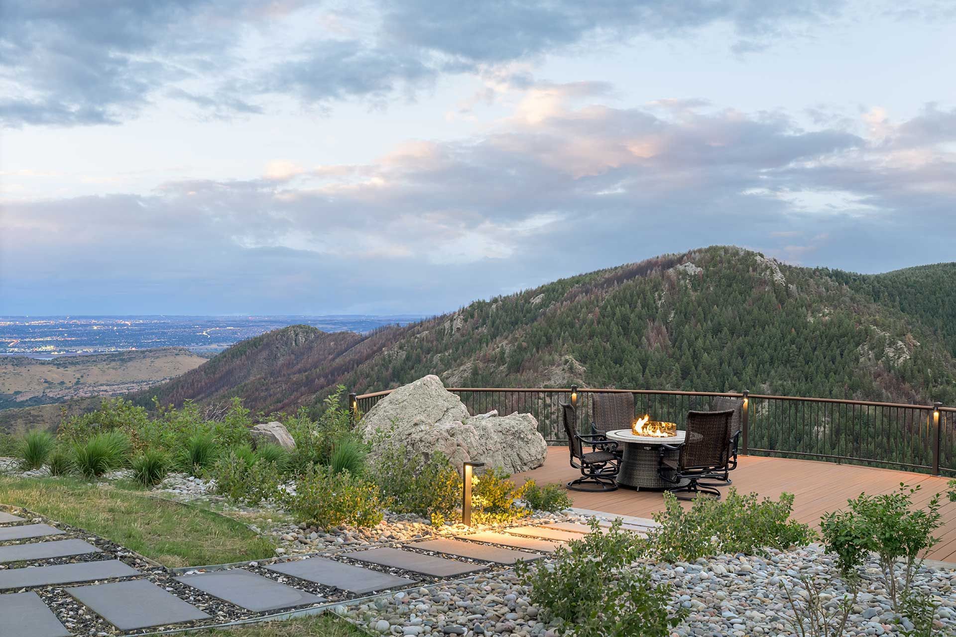 An outdoor patio with a fire pit overlooking mountains and a valley at dusk.