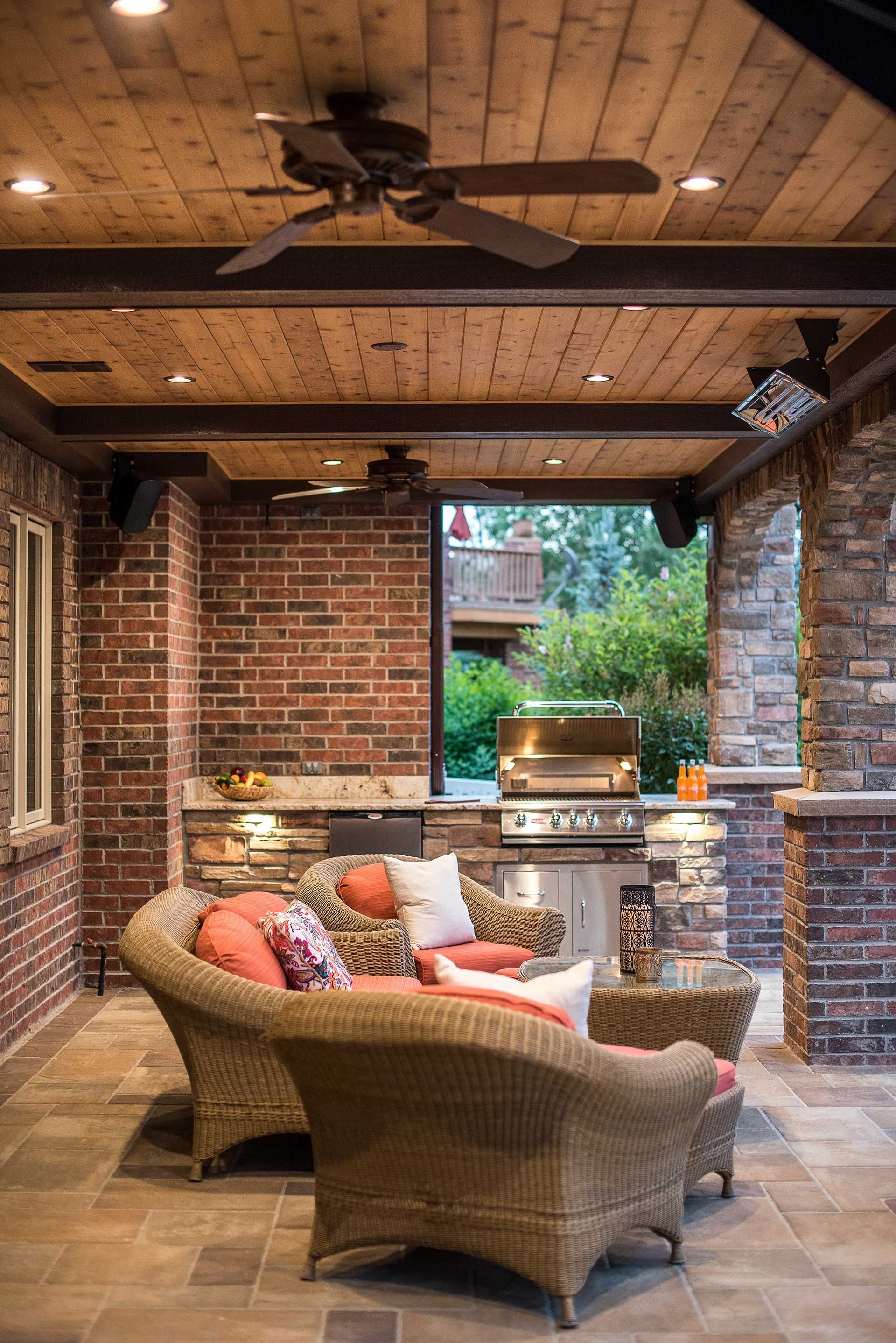 Covered outdoor patio with wicker seating, brick walls, stone flooring, and a built-in kitchen area.