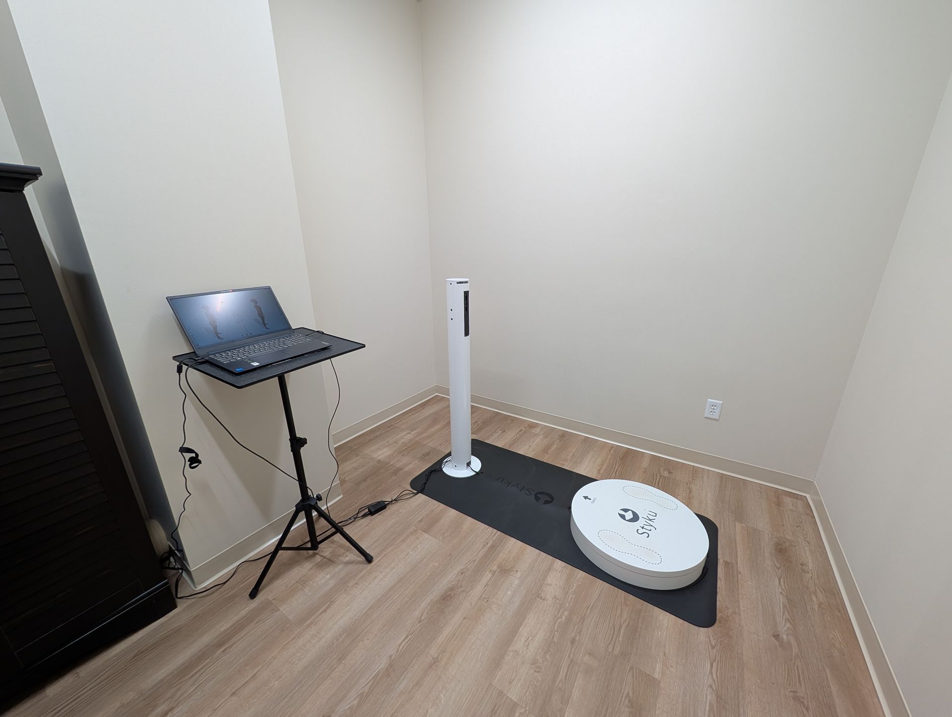 A small room with a laptop on a tripod, scanner device, and black cabinet.