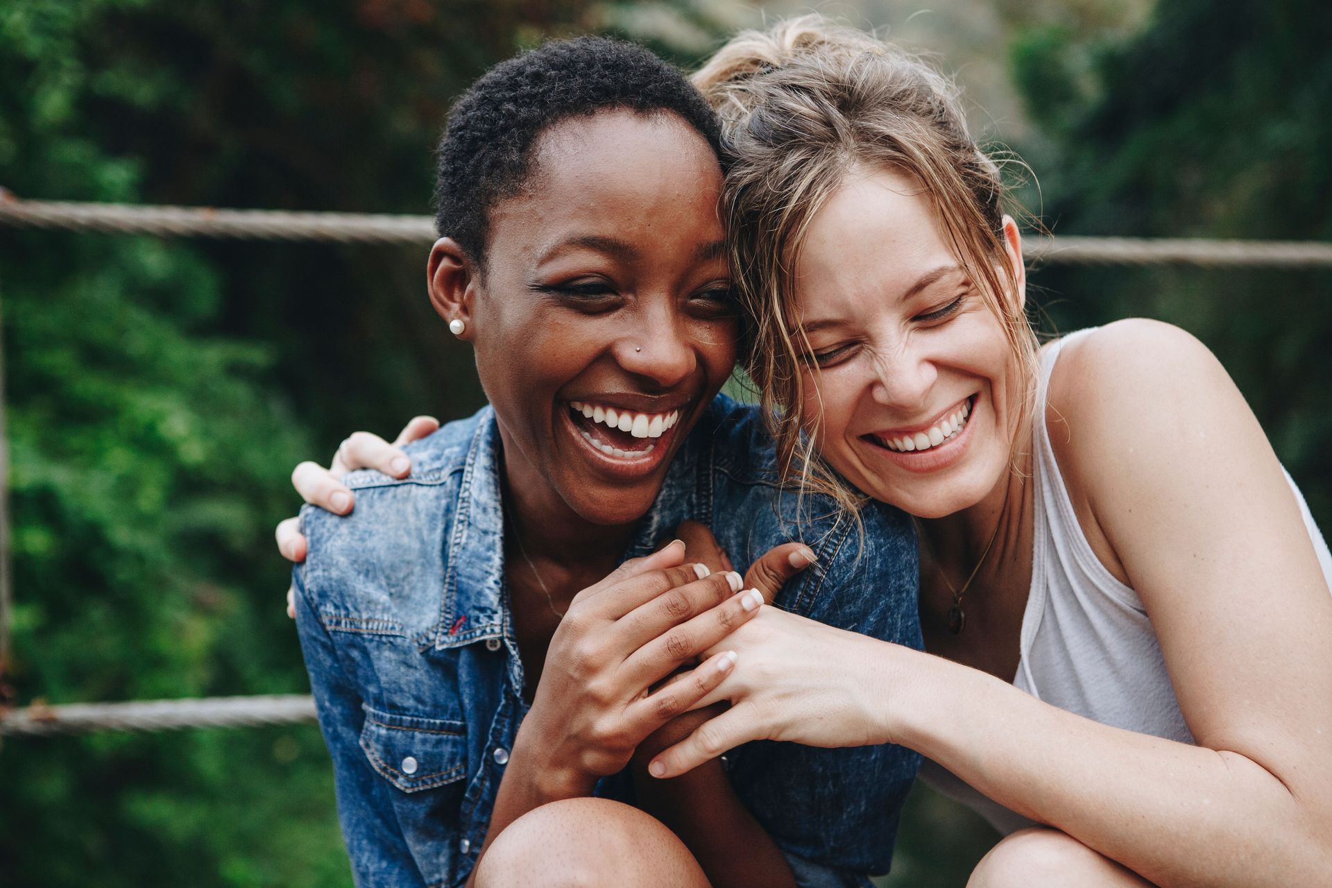 Two women laughing, arms around each other; one Black, one white, outdoors.
