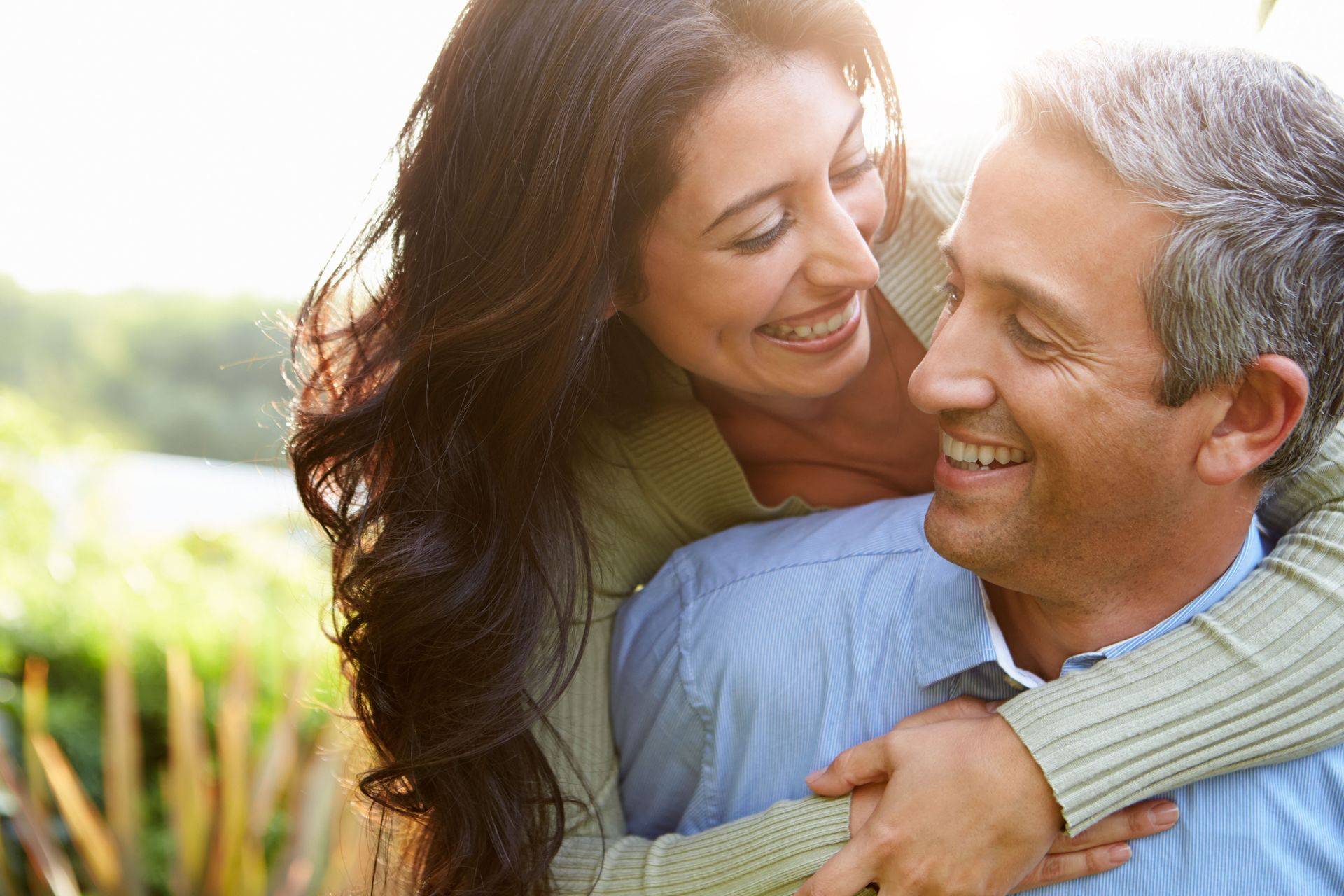 Woman hugging a smiling man outdoors; both are smiling.