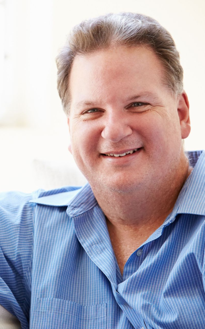 Smiling man in a blue button-down shirt. Soft lighting, neutral background.